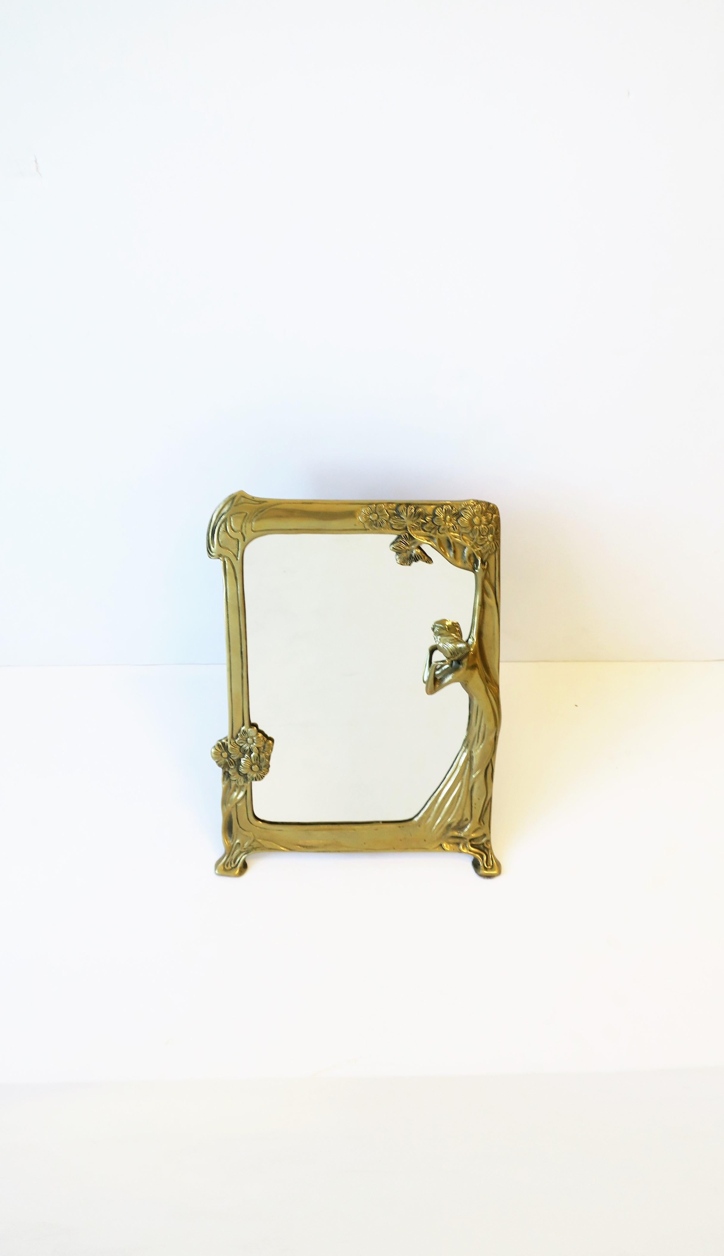 A brass vanity table mirror in the Art Nouveau style, circa late 20th century. A solid brass frame featuring women and flowers. A great piece for a vanity area, walk-in closet, bathroom, etc. Piece measures: 10