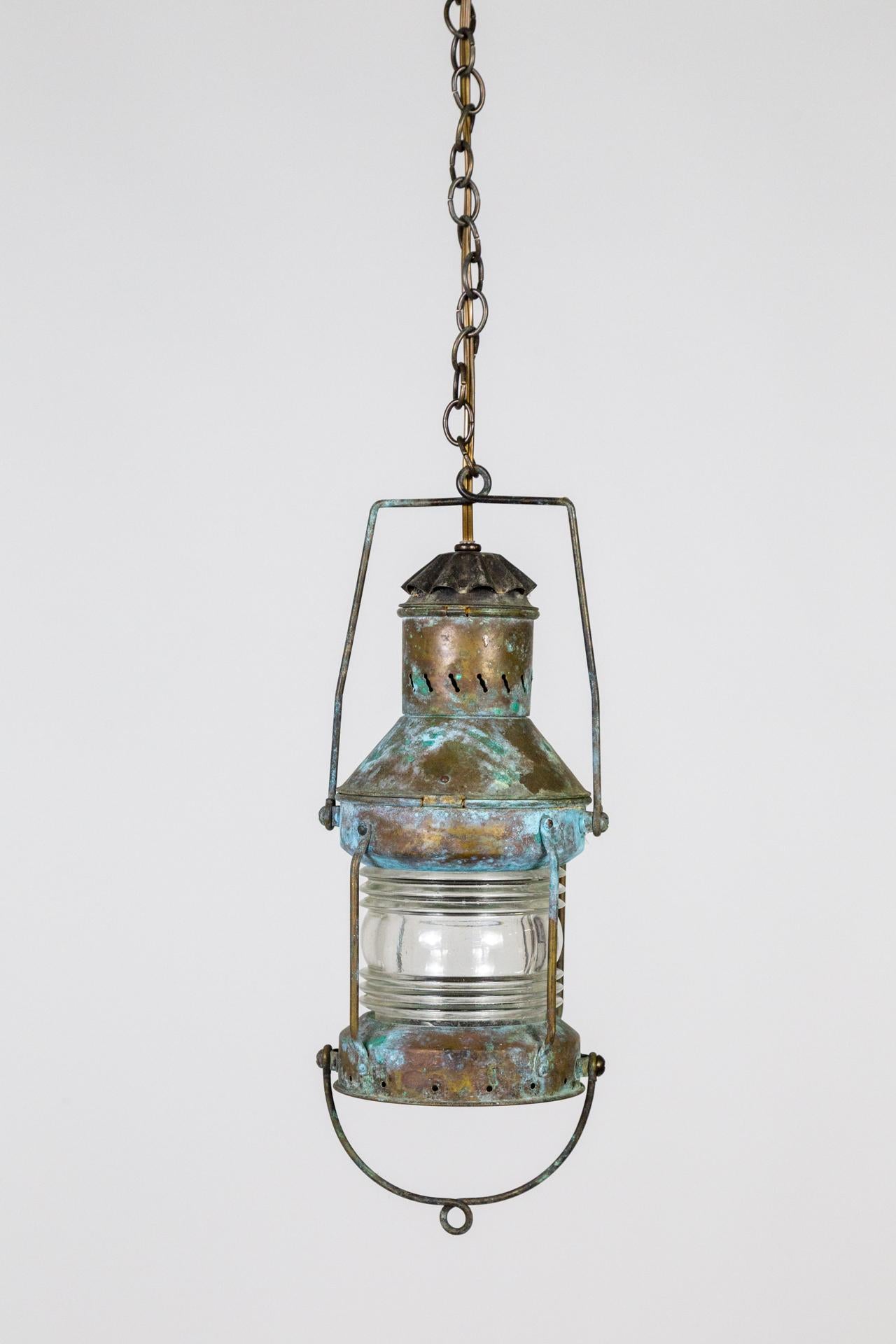 An early 20th-century hanging lantern in cylindrical form with beautiful diffusion from the Fresnel glass. With a remarkable antique brass, blue,  and verdigris patina and a long chain. Newly wired and made into a hanging light. 6