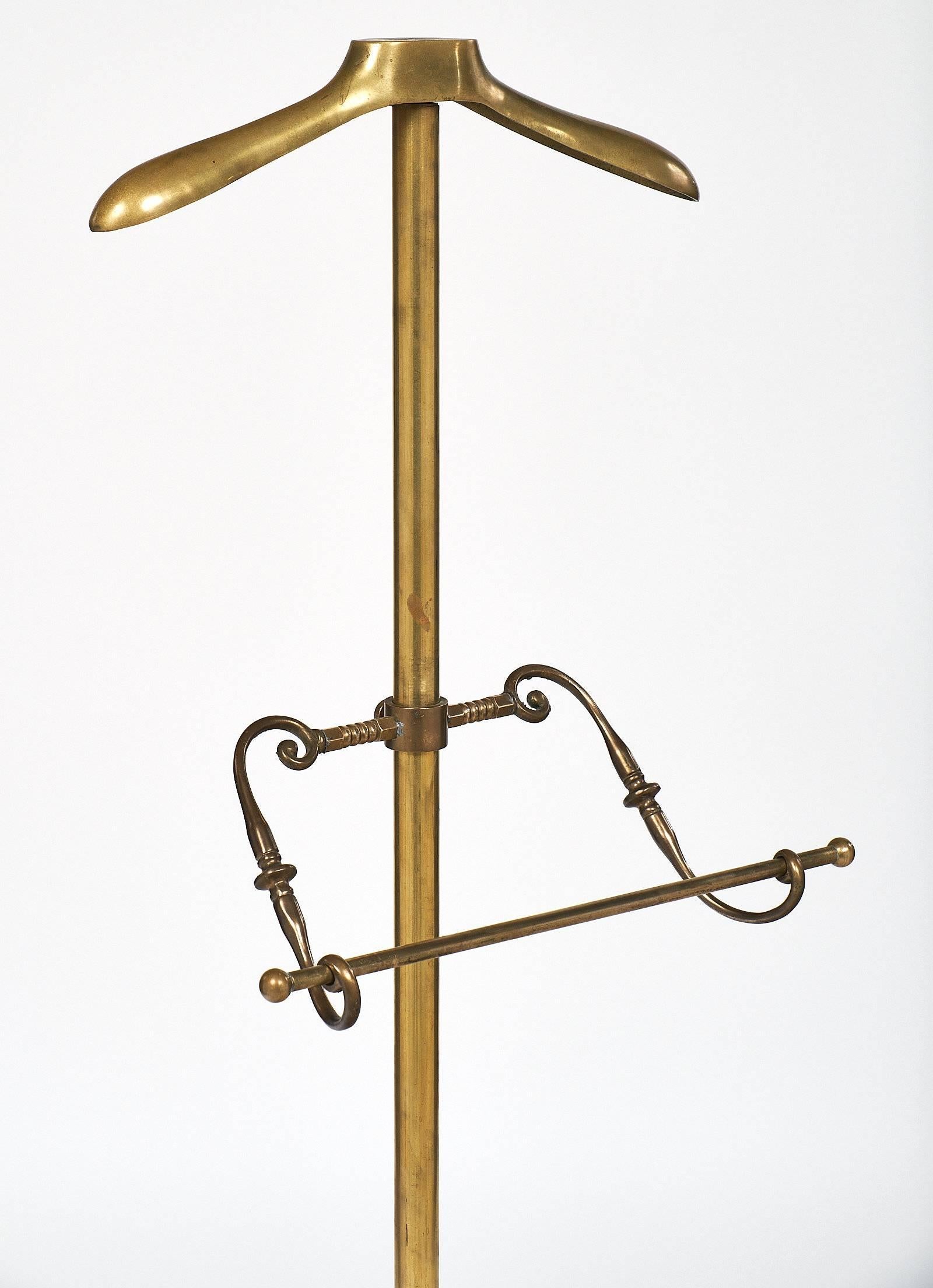 French vintage brass valet. The centre stem ends with a hanger at the top, and at waist height is a towel rack. The base features an embossed plate with tripod feet.