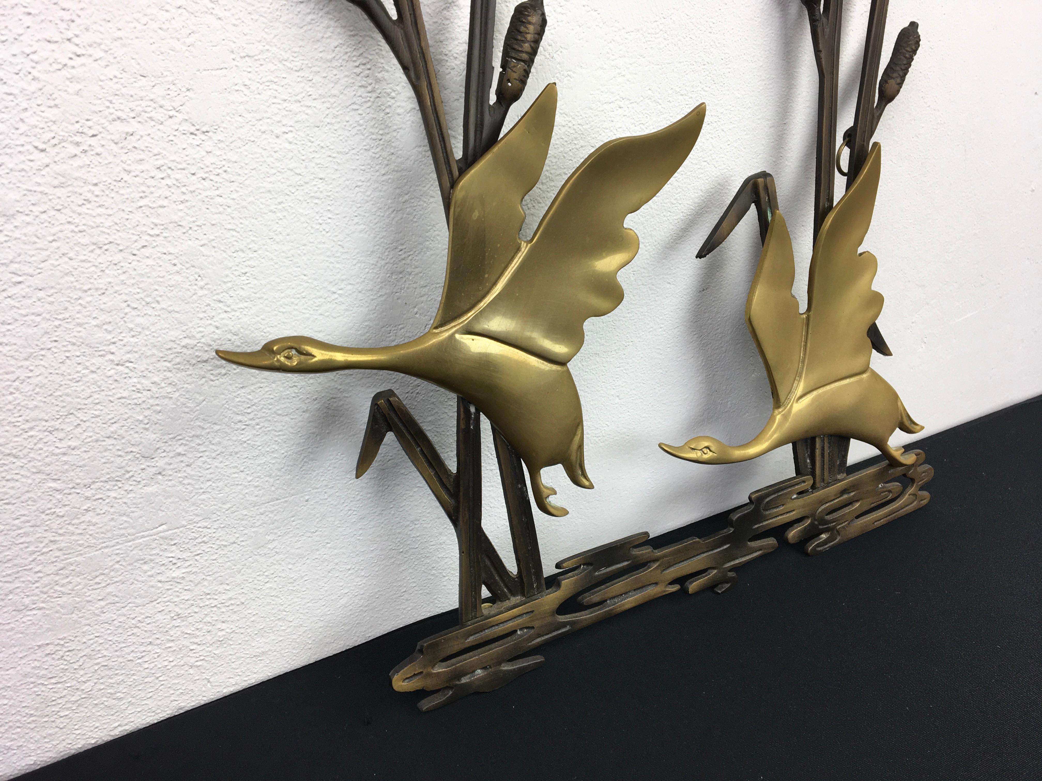 1960s wall decoration with duck birds. This wall sculpture is made of brass or messing with bronzed metal. A landscape in nature with 2 flying ducks and cattail plants at the back. The brass of this stylish wall decoration has not been polished yet,