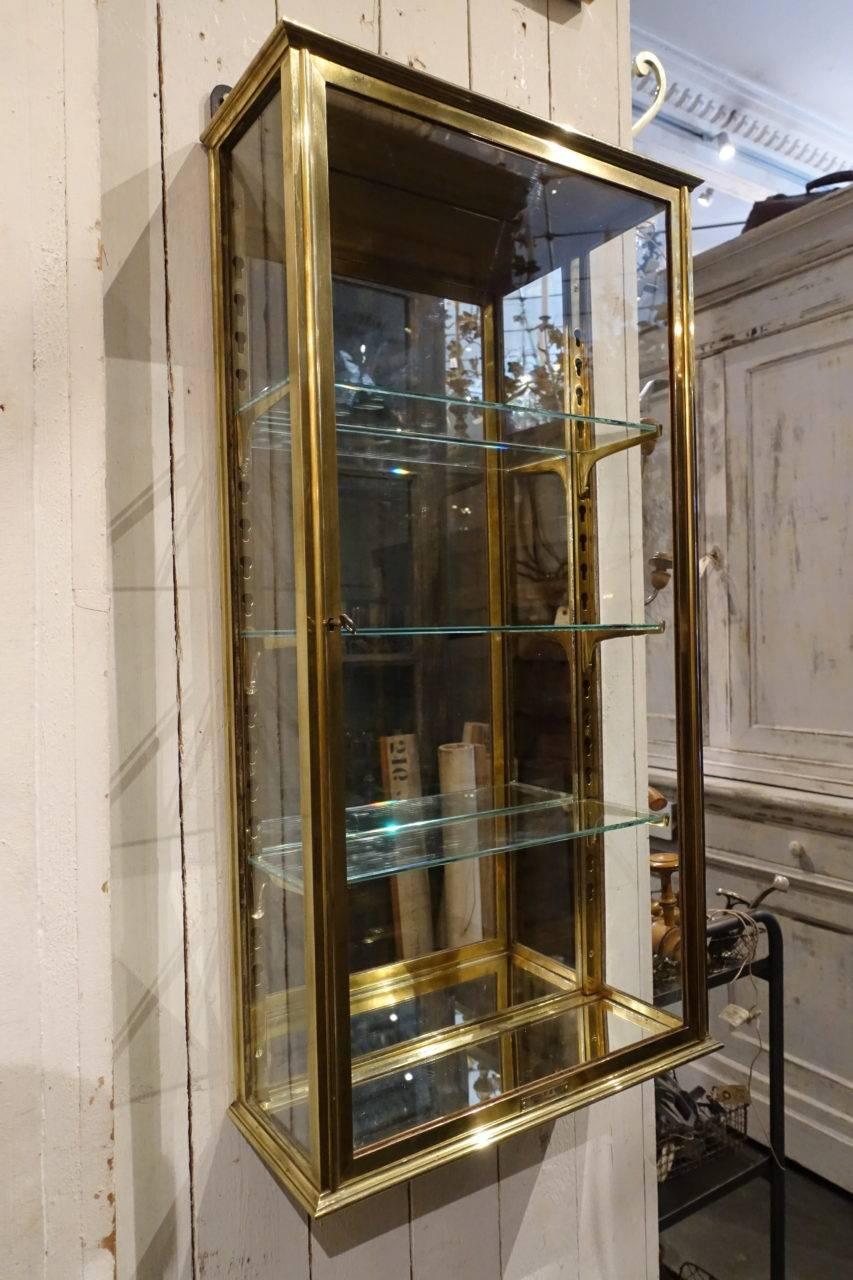 Super vintage French wall vitrine cabinet, made in brass, with original keys and three glass sealves, and their cast brass adjustable brackets. Provenence – part of a boutique’s inventory, with the producer’s name clearly indicated on the base.
