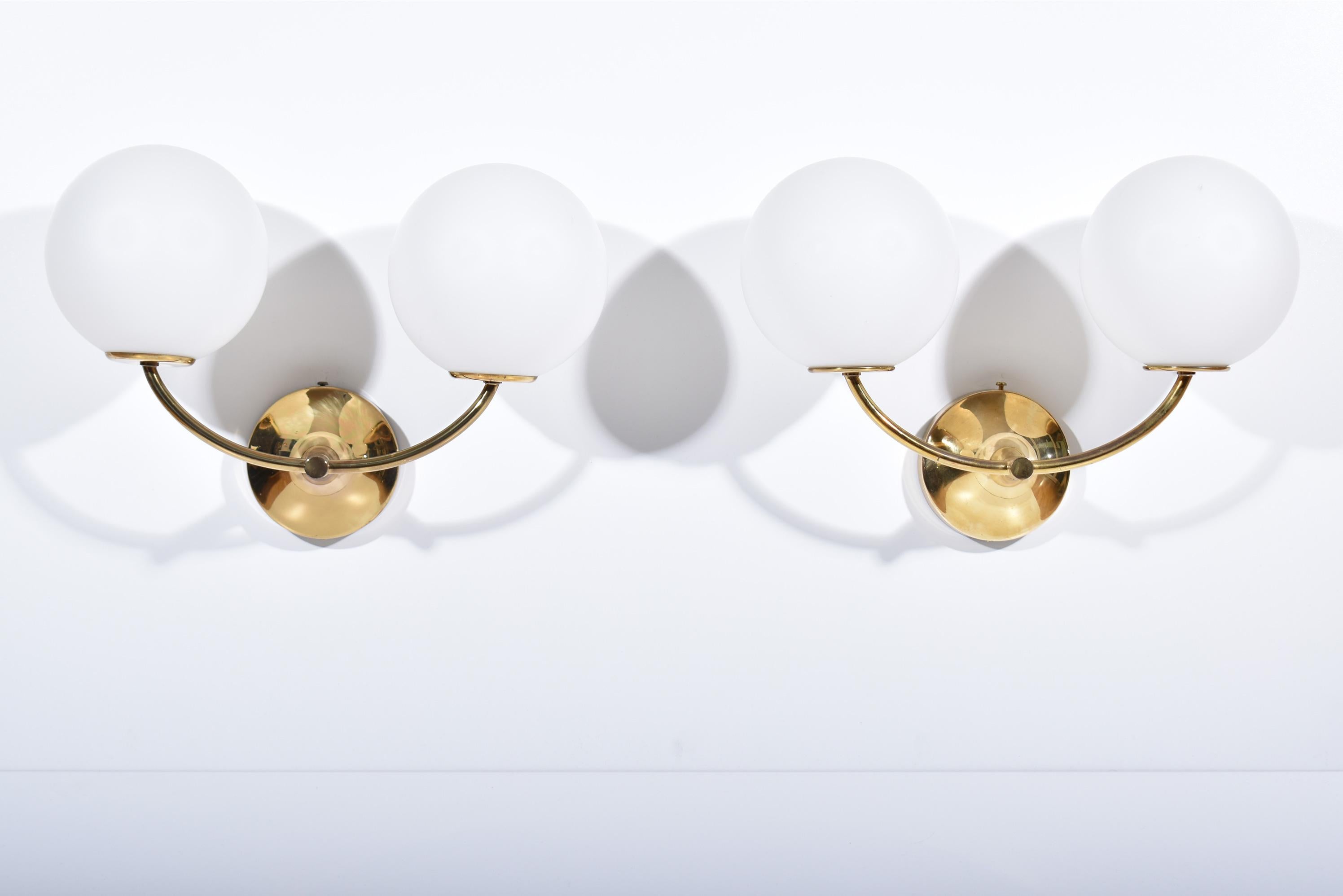 Set of four brass sconces, each with two glass globes.
Original design, at the crossroads of Art-Déco, Bauhaus and Mid-century modern.
Simple and elegant, it was designed by E.R. Nele, but is usually attributed to Max Bill. 
It was produced in