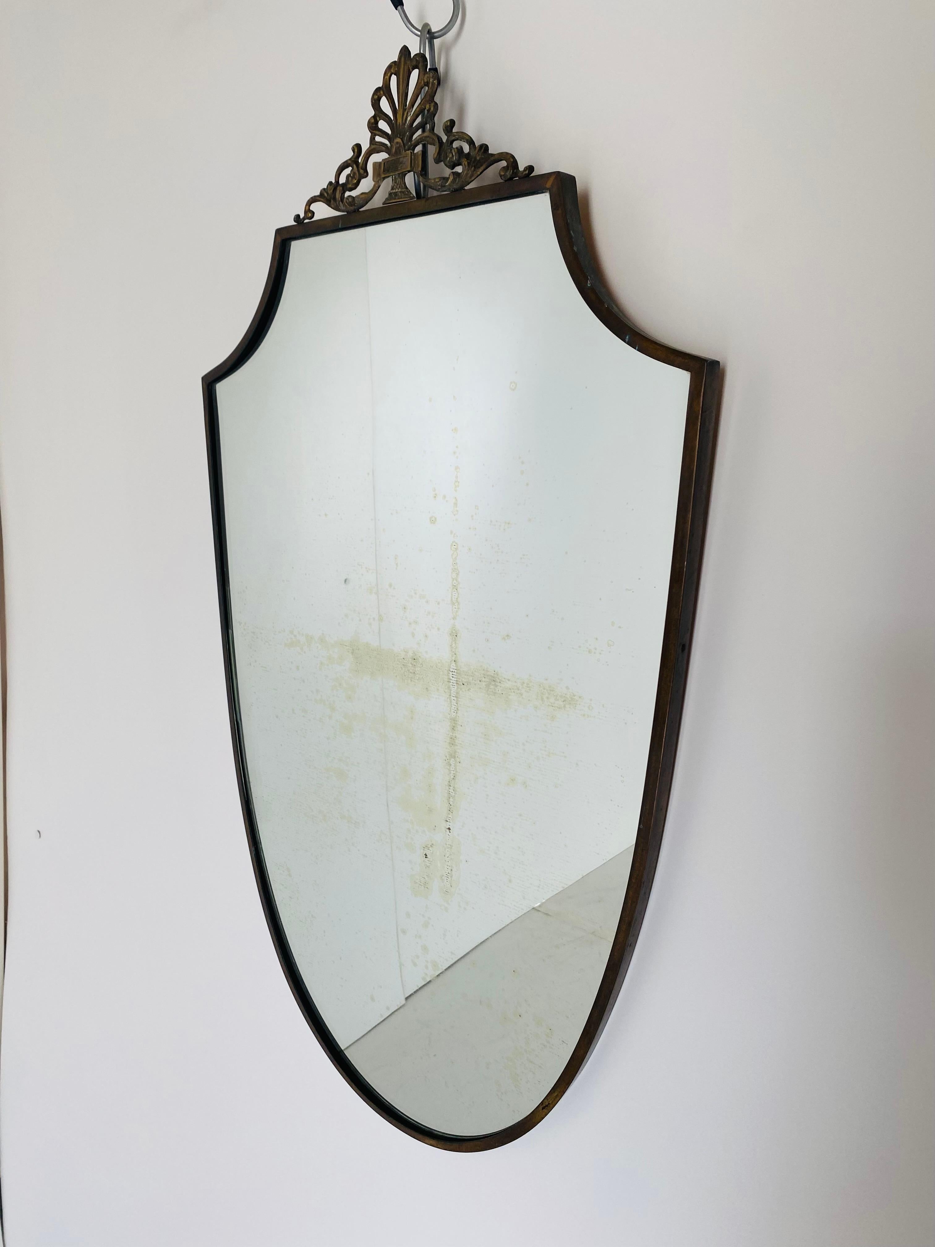 Brass wall mirror, 1940s, Italy.
A 1940s brass wall mirror with elegant curved structure and decorative details on the top. 
Original glass with beautiful signs of the time on it. Very good conditions.
 