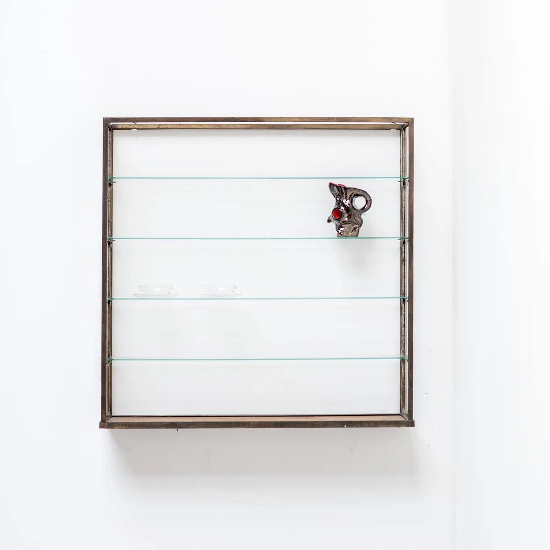 Elegante mensola da parete con struttura in metallo minimalista e quattro ripiani in vetro. La combinazione di linee sottili in metallo e vetro trasparente crea una presenza leggera e architettonica, ideale per esporre piccoli oggetti, ceramiche o