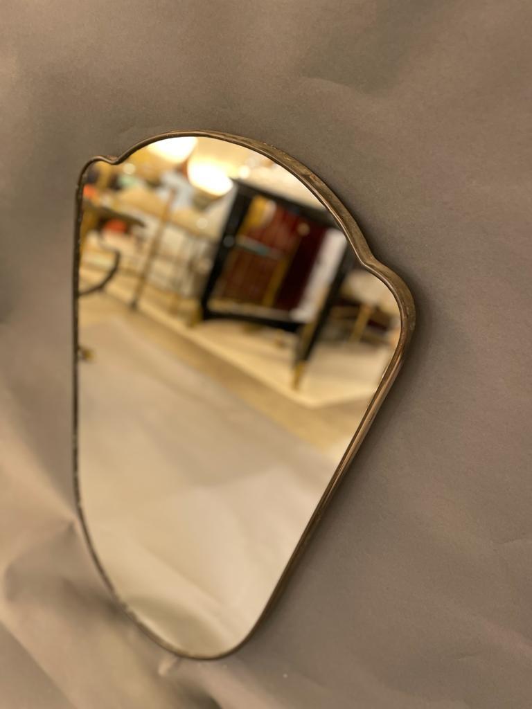 Wall mirror with brass frame, made in the 1950s in the style of Giò Ponti. The shaped frame, is with original patina. The Mirror has some signs of ageing 
in good vintage conditions