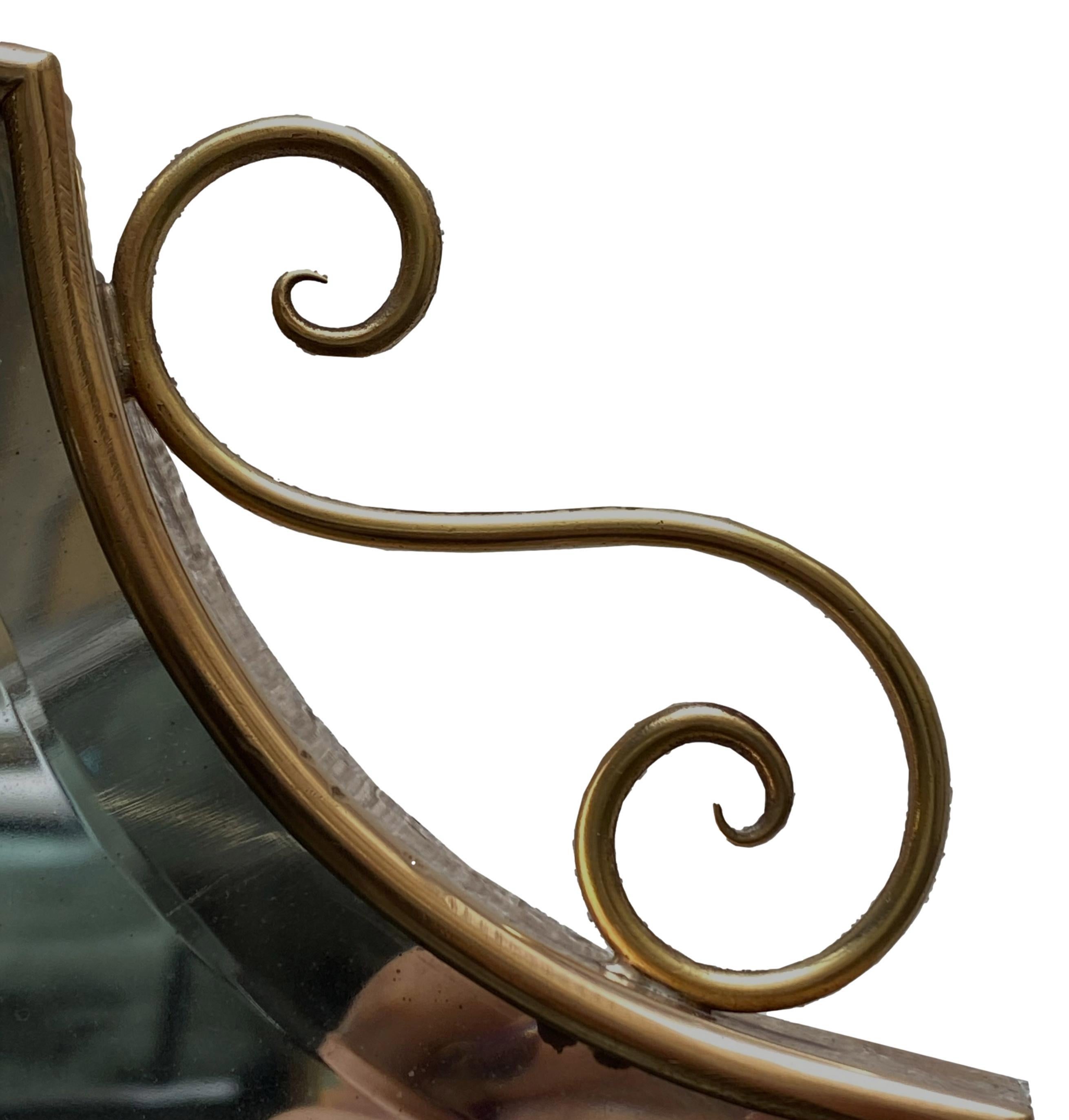 Wall mirror with brass frame, made in the 1950s in the style of Giò Ponti. The shaped frame, has workings on the upper part. Mirror with considerable signs of ageing on the lower part.
 