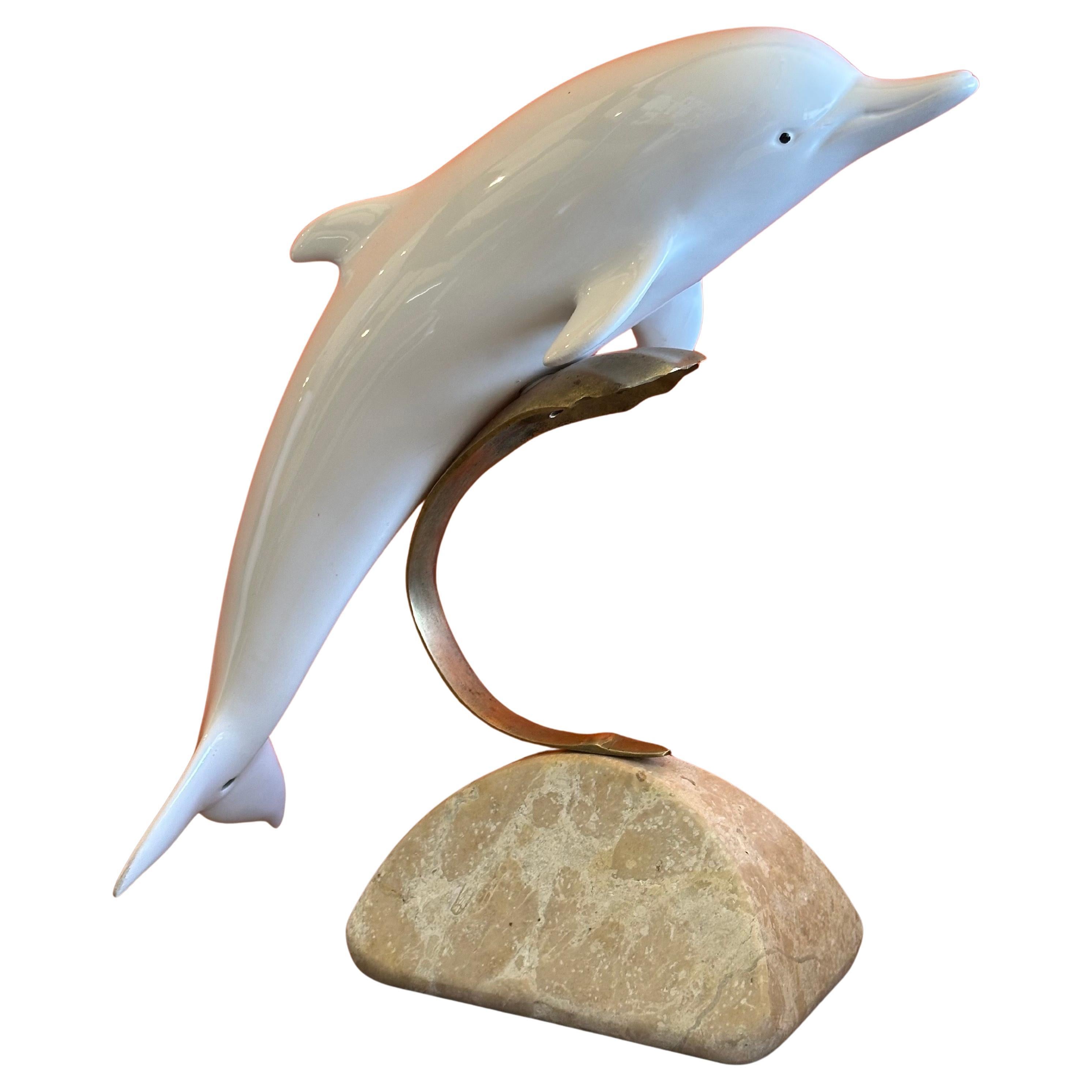Bellissima scultura di delfino in ottone con onde di porcellana di Hollywood Regency su base di marmo di Bijian, circa anni '80.  La scultura poggia su un'onda in ottone curvo e misura 10,5