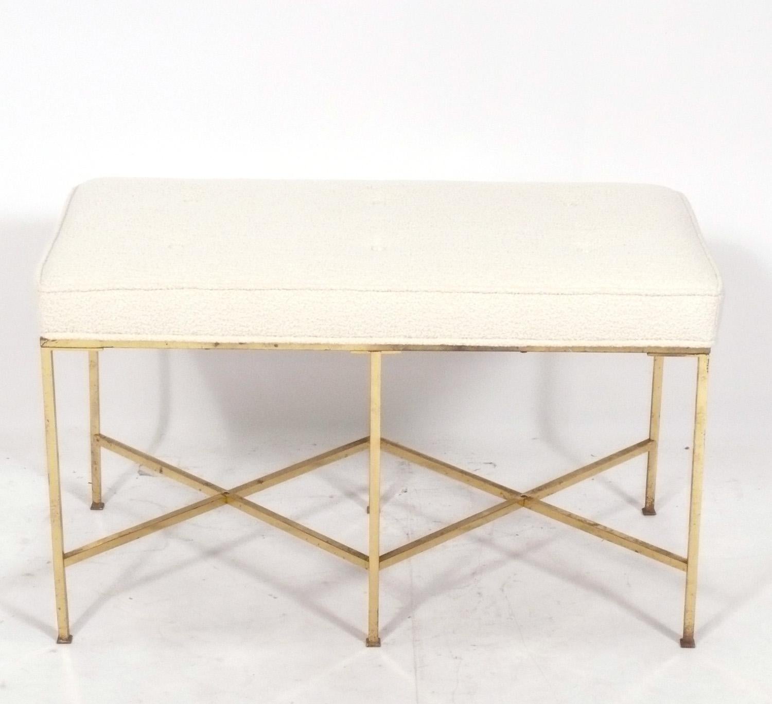 Sculptural X-based brass bench, in the manner of Paul McCobb, American, circa 1950s. It retains its original distressed patina to the base, and has been newly reupholstered in an ivory colored upholstery.
