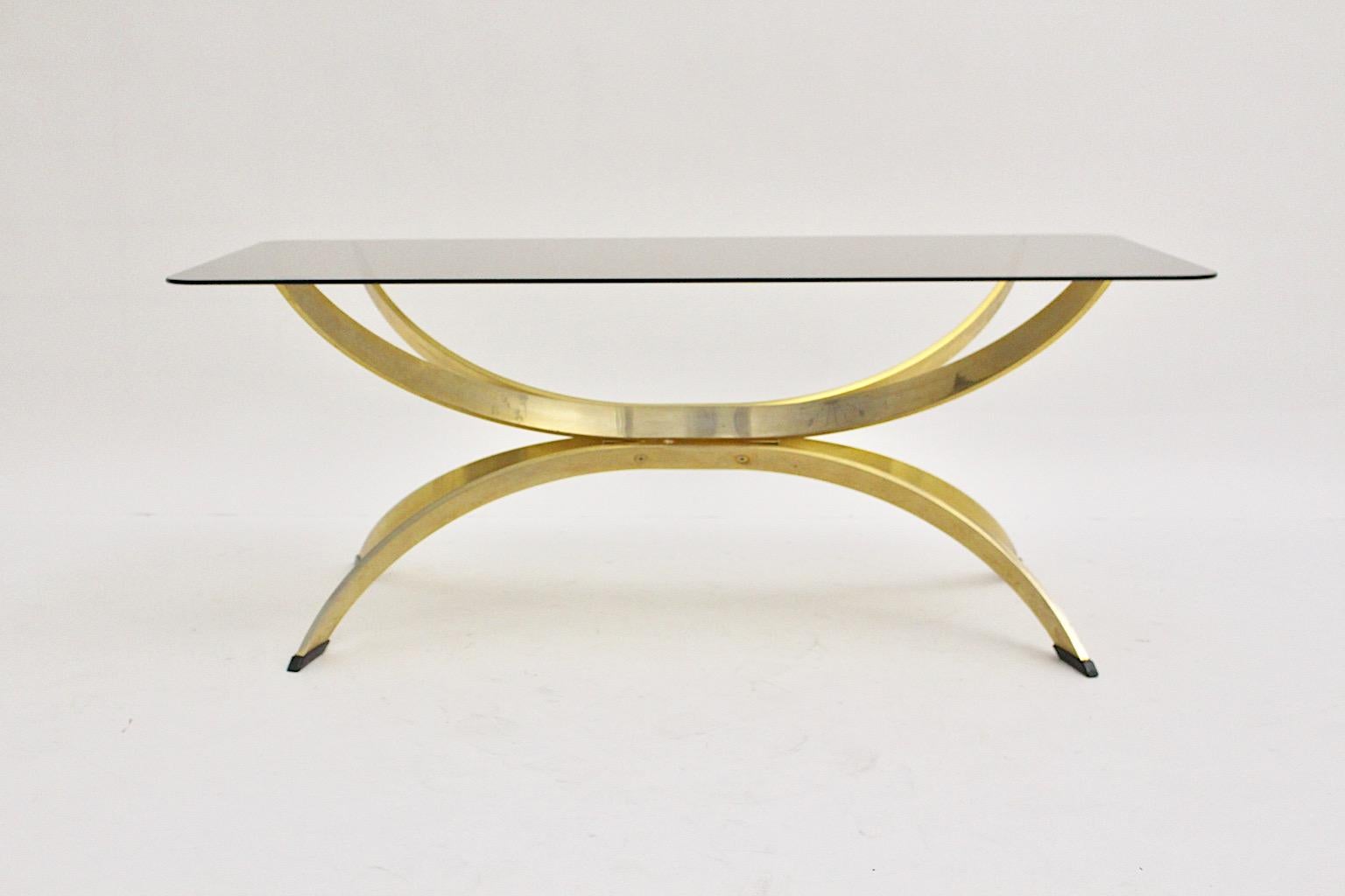 Brassed metal vintage coffee table or sofa table in sculptural shape designed 1970s with a rectangular smoked glass plate and 4 black sabots.
The brassed metal base shows powerful movement in its sculptural form while the smoked clear glass plate