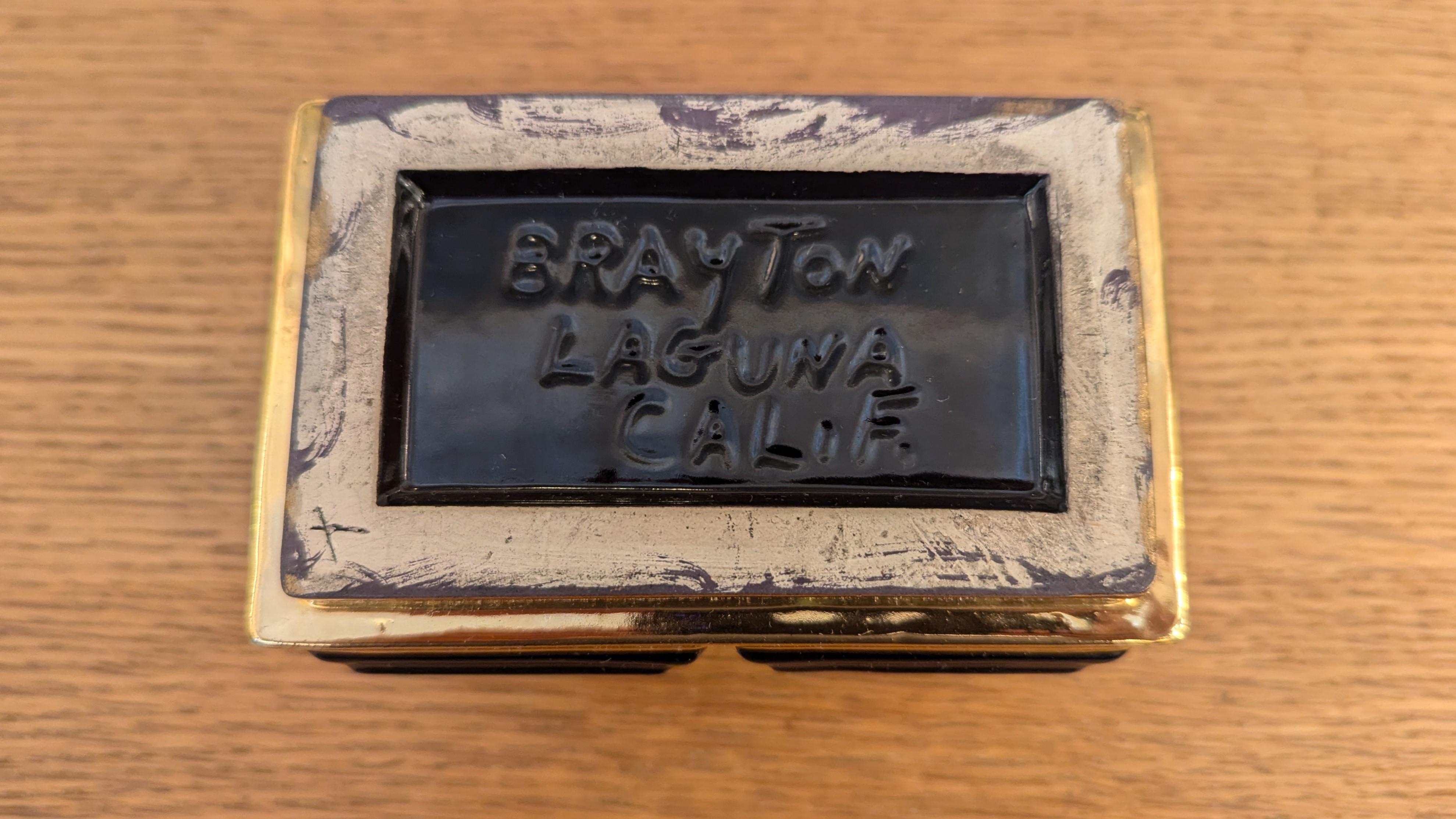 Caja de Cerámica de Mediados de Siglo Brayton Laguna.  Rico esmalte negro macizo acentuado con esmalte dorado metálico que tiene una sencilla forma rectangular con detalle circular.  Diseño Art Decó de mediados de siglo hecho a mano. La parte