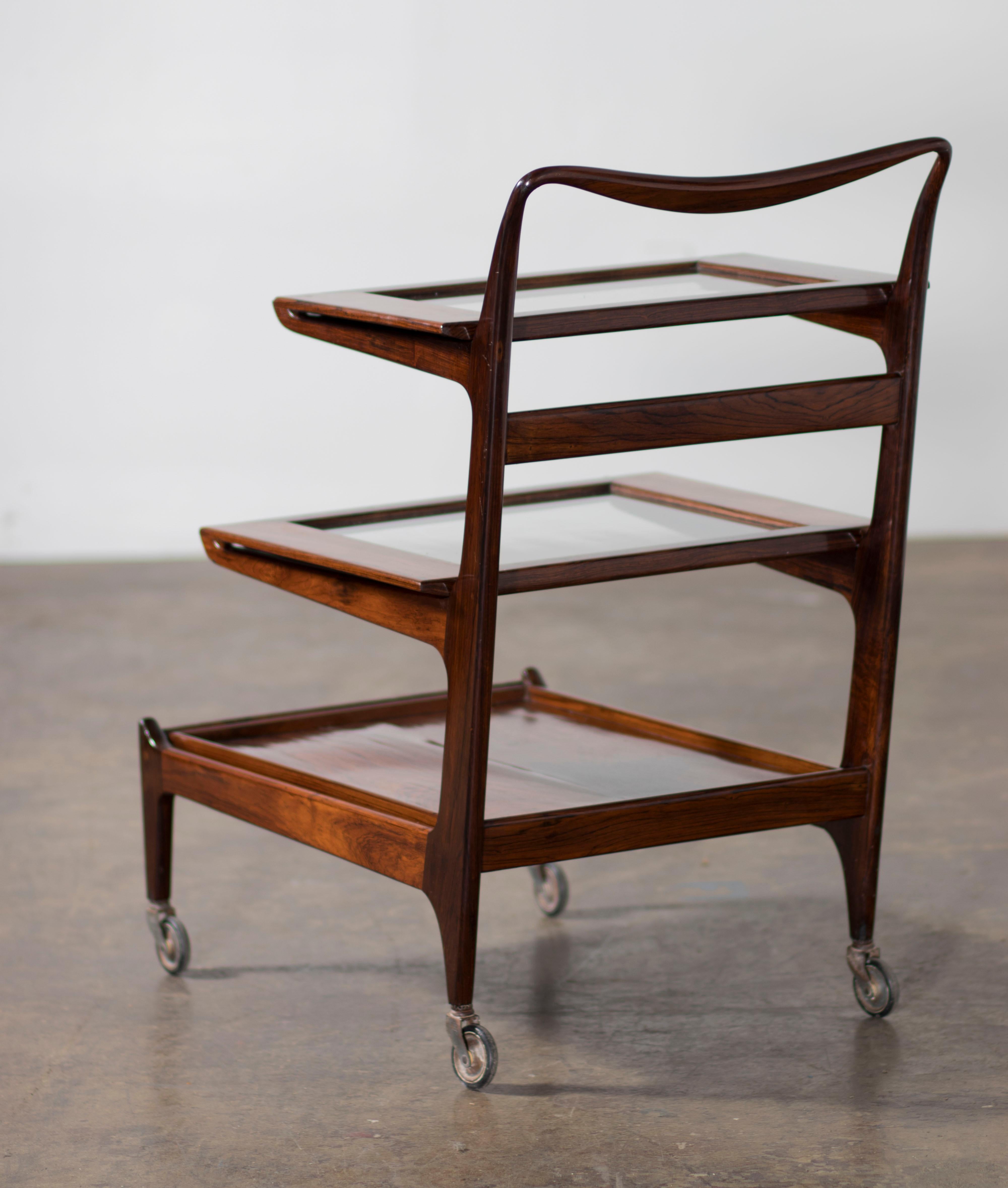 Designed by Carlo Hauner and Martin Eisler, the bar cart is made of Rosewood, Glass, and Steel. Composed of three removable serving trays and steel casters for Forma S/A Móveis e Objetos de Arte, Brazil, São Paulo, 1955.  