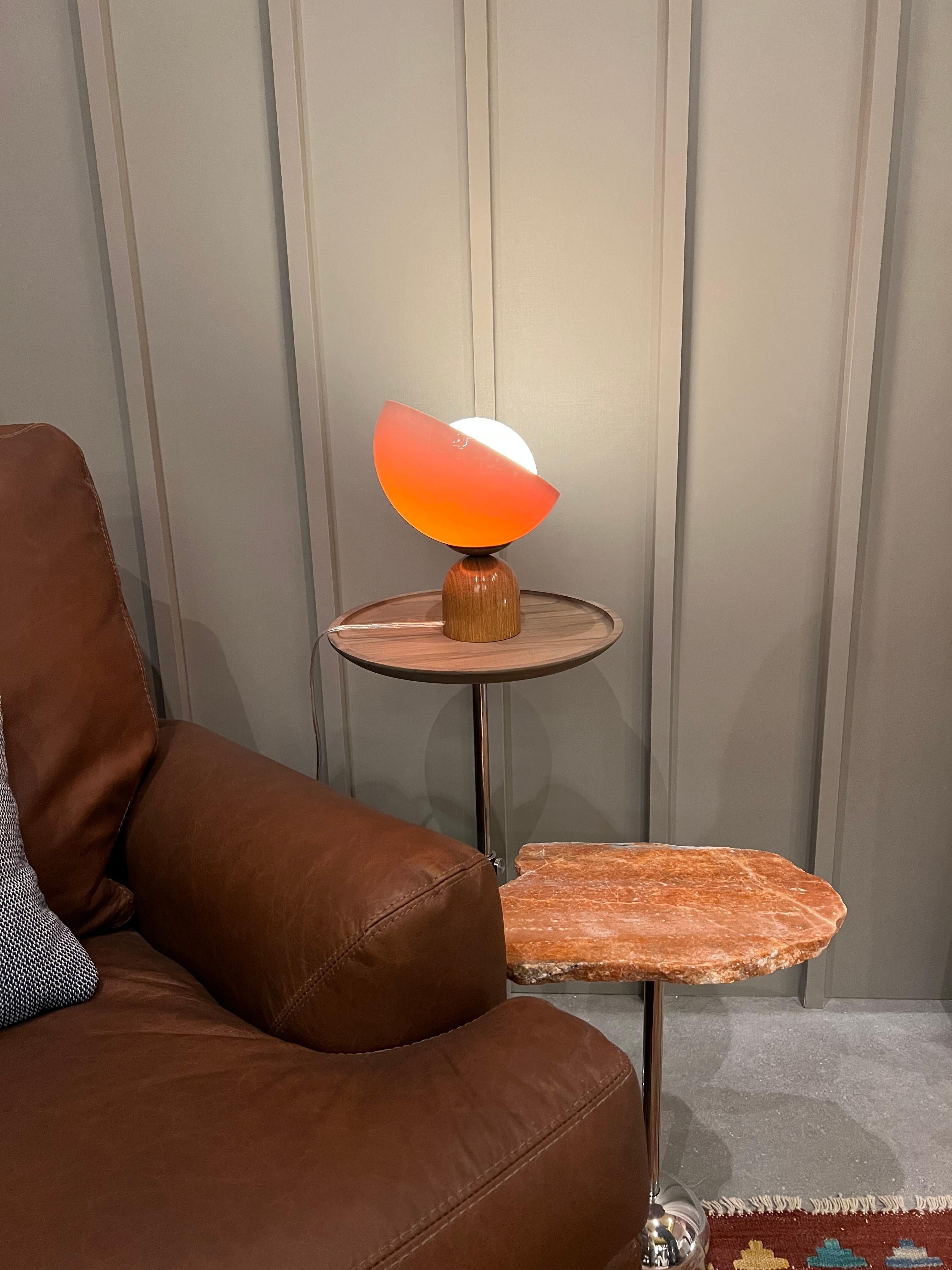 This table lamp is named Lichia. 
The product consists of a round acrylic diffuser and a wooden base.
The base is made of wood, shaped in a rounded design and with a varnish finishing, which gives the piece a shiny aspect.
The diffuser is made of