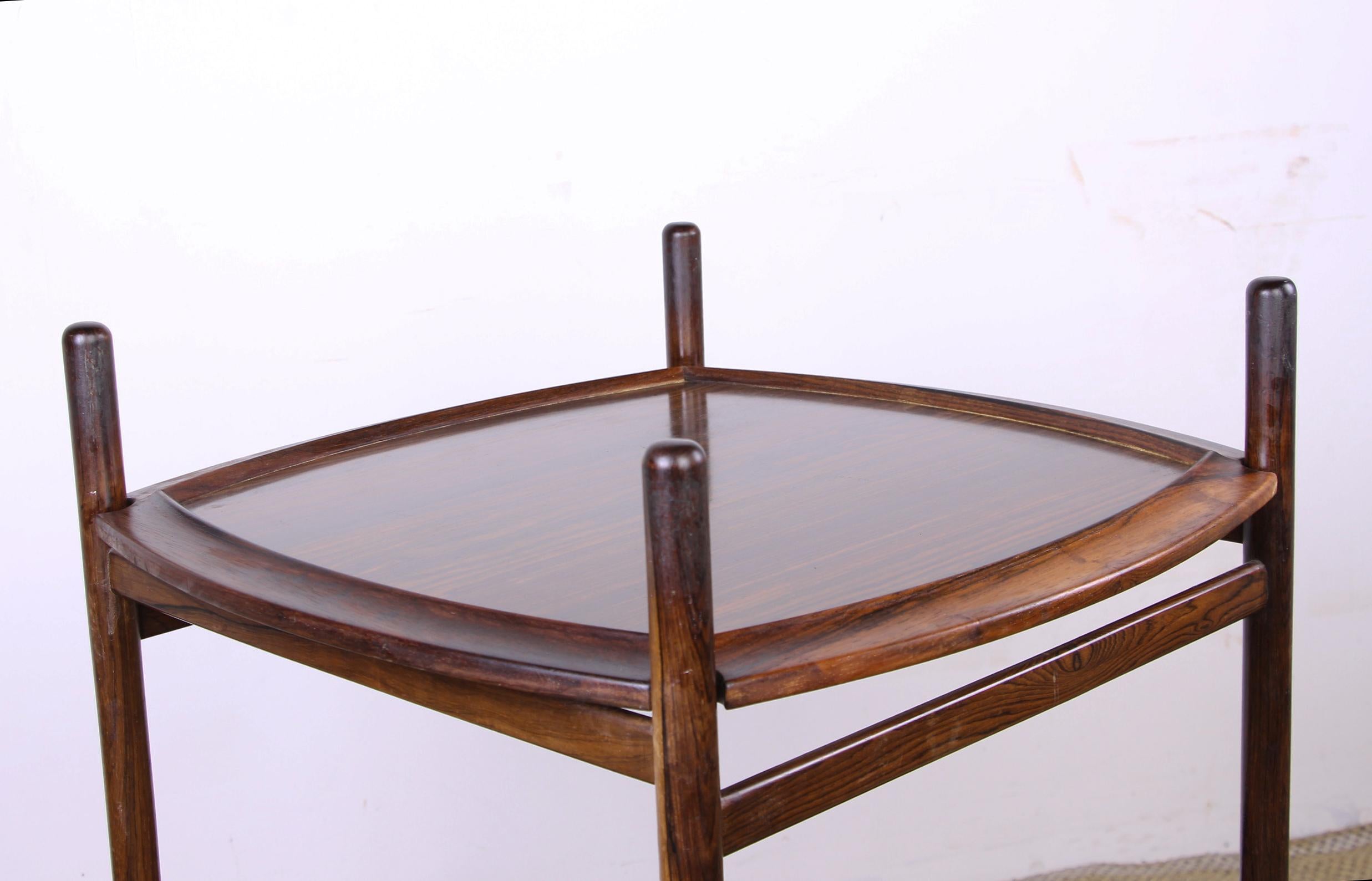 Rolle è un ingegnoso tavolo o carrello da portata con 2 vassoi impilati che si possono facilmente ribaltare. 
Un lato in palissandro e un lato in formica color crema. 
Le 4 gambe alte gli conferiscono una notevole eleganza. Una lavorazione molto