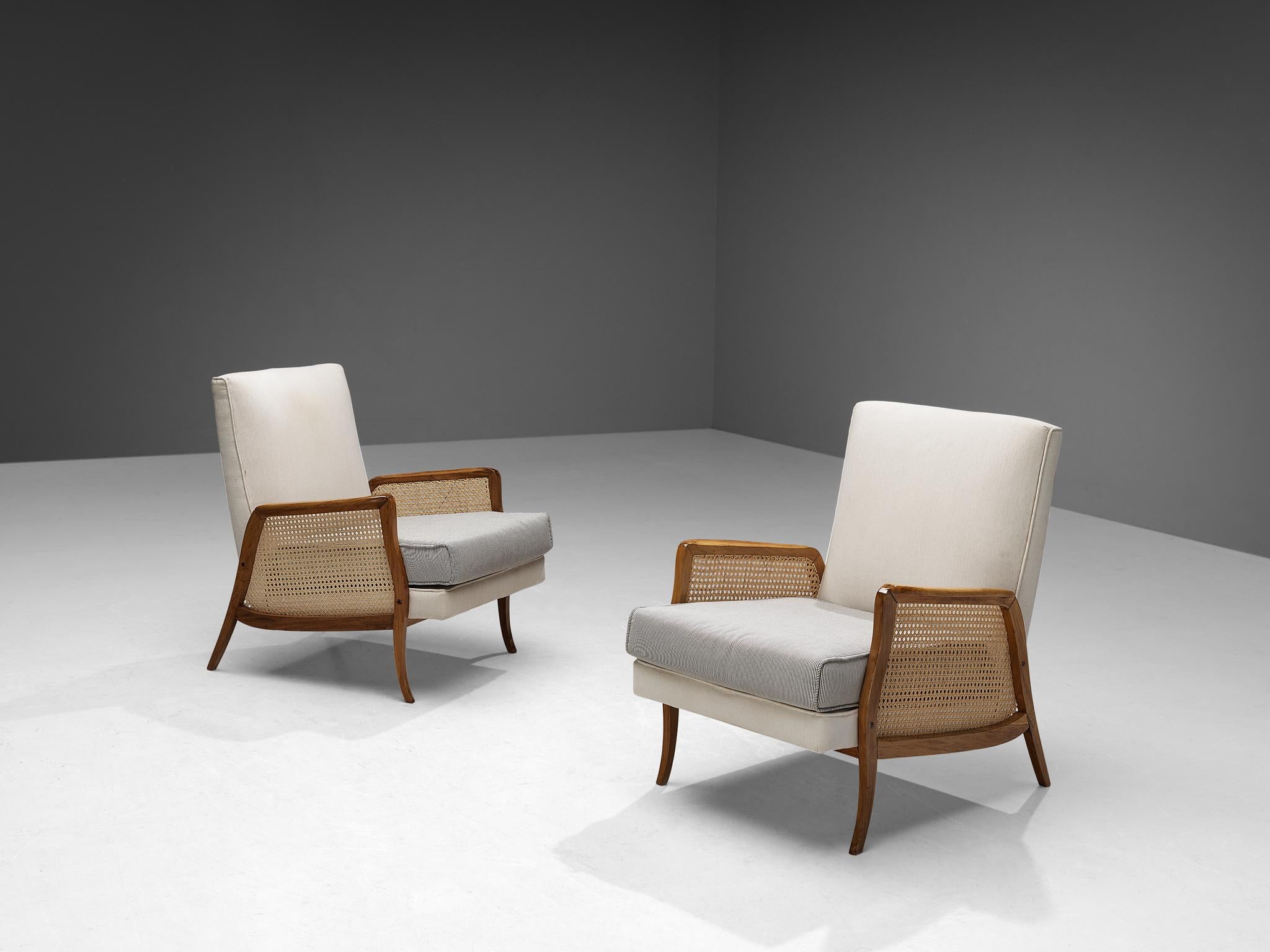 Pair of lounge chairs, walnut, fabric, cane, Brazil, 1950s.

The style of these Brazilian armchairs is simple and understated, where clear, fluent lines are allowed to emerge in the design. The wooden frame in walnut embodies striking curvaceous