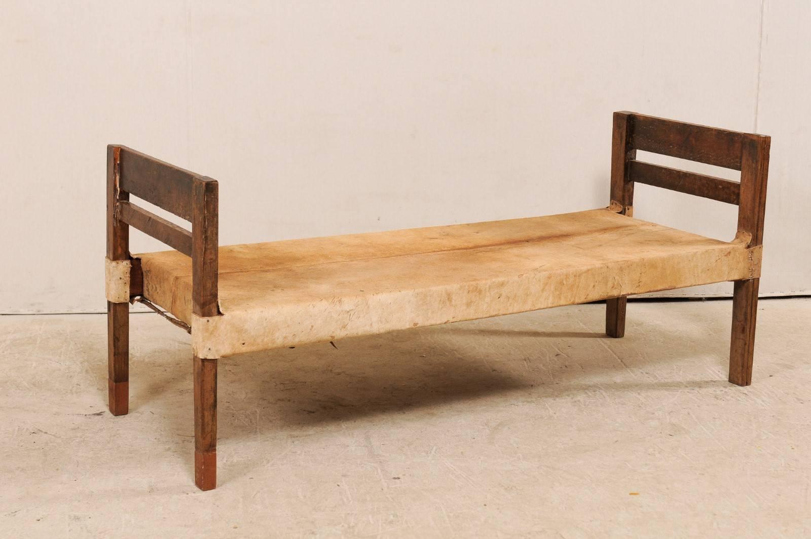 A Brazilian mid-20th century single daybed with cowhide and wood frame. This vintage Brazilian daybed features wooden slatted foot and headboards, which extend to make up the square shaped legs. The bed is upholstered in a honey colored cowhide with