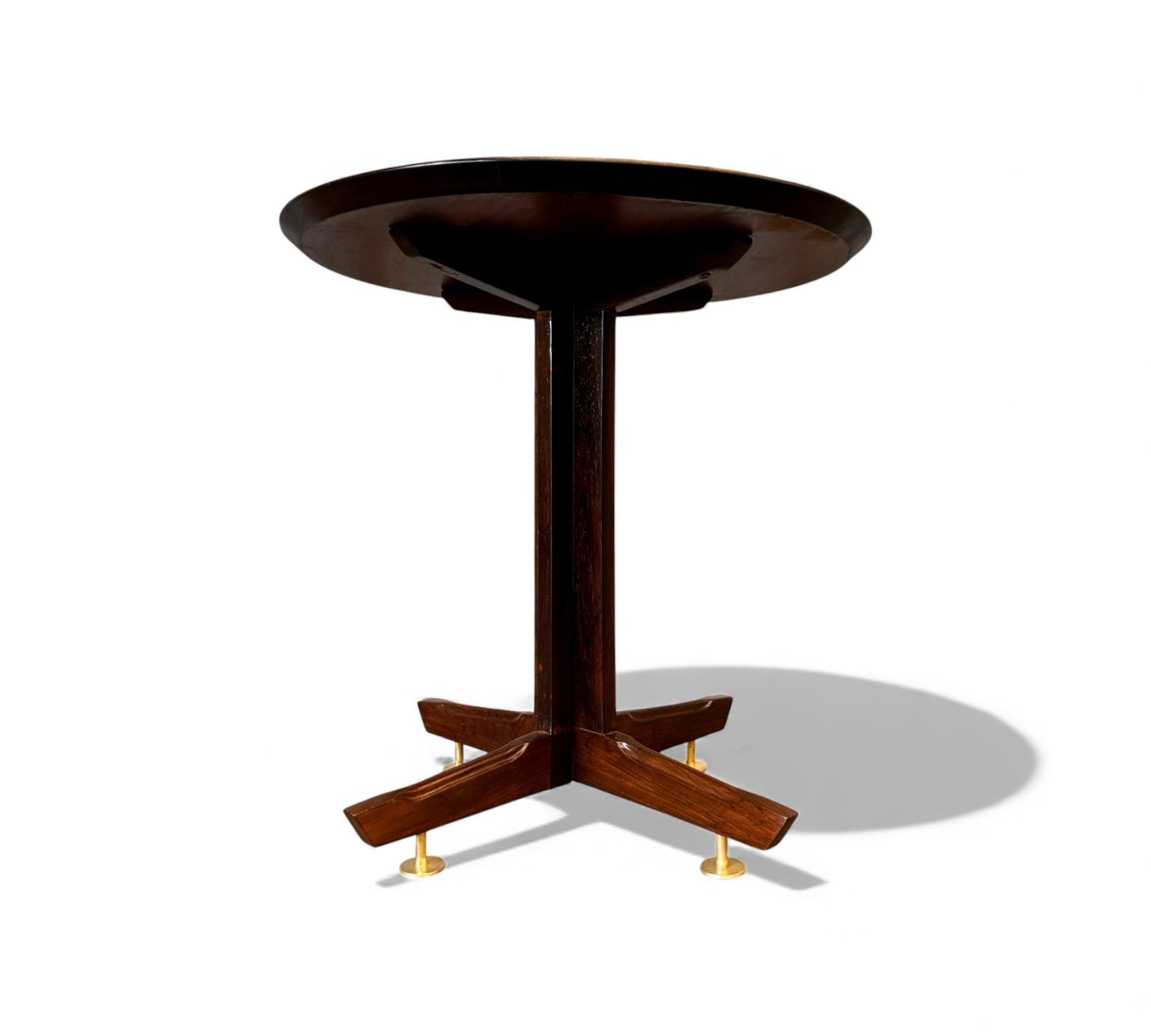 Cette table d'appoint brésilienne des années 1960 est fabriquée en bois dur brésilien massif et présente un plateau rond et épuré soutenu par une colonne centrale et une base à quatre points. Les pieds coiffés de laiton ajoutent un détail simple et