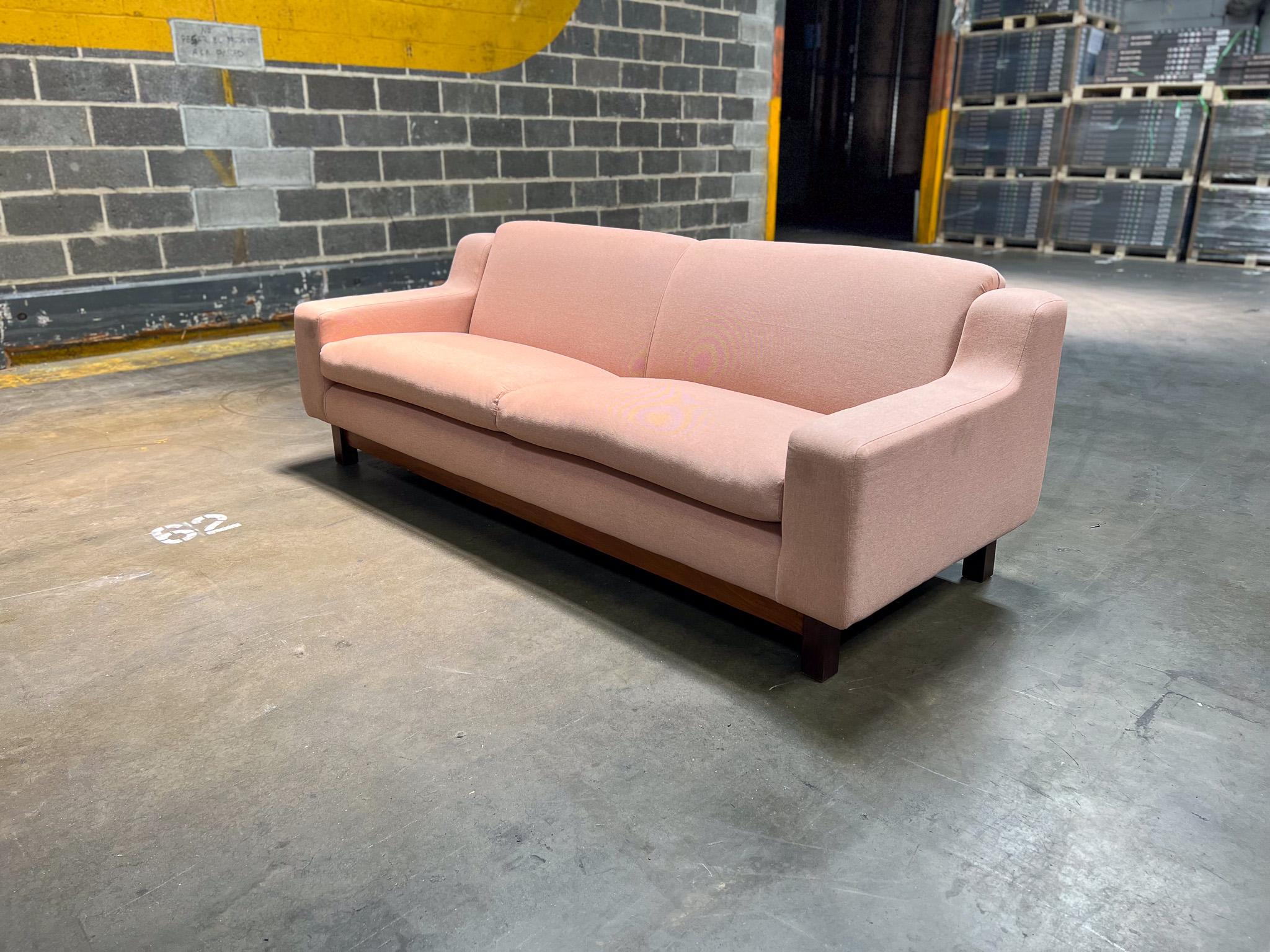 Dieses heute erhältliche Mid-Century Modern-Dreisitzer-Sofa besteht aus einem massiven Hartholzrahmen mit lachsfarbener Leinenpolsterung. Der Sockel ist aus brasilianischem Palisanderholz, auch bekannt als Jacaranda, gefertigt und weist bunte