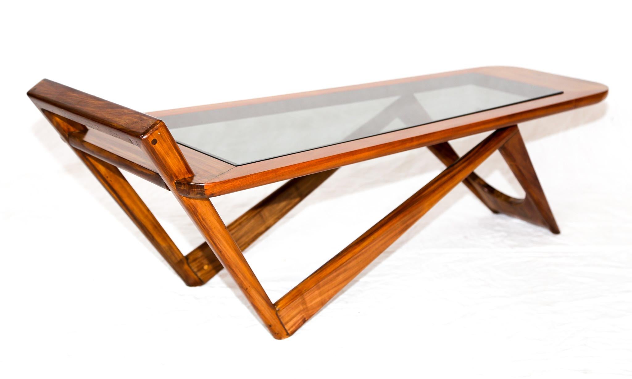 This coffee table by Pierre Weckx is made with Brazilian hardwood and features a glass piece that is attached to the tabletop. The wood on this piece has been refinished and is in excellent condition. This coffee table has a very unique design to