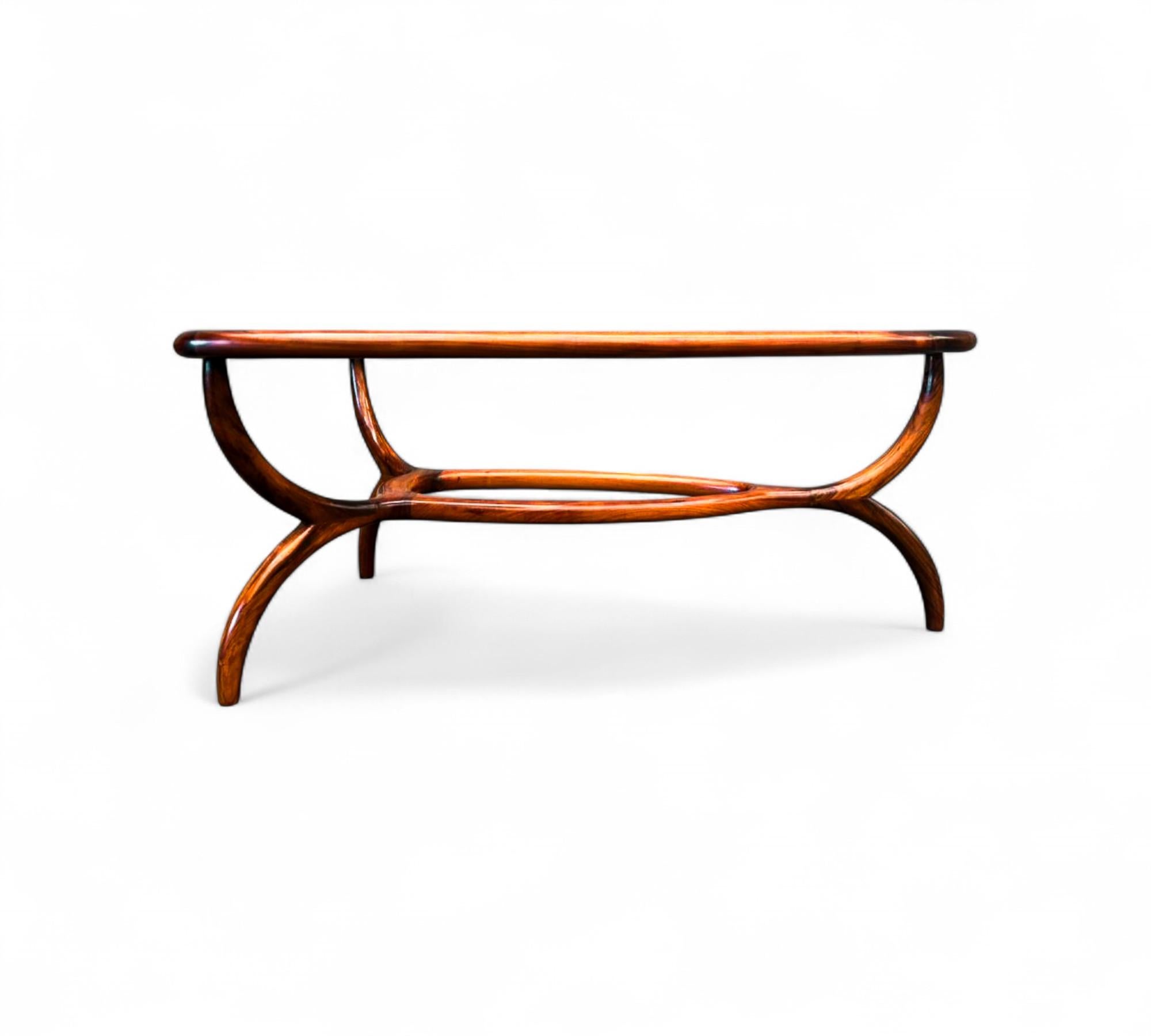 Elegante table basse sculpturale conçue par Giuseppe Scapinelli, fabriquée en bois dur massif avec un cadre magnifiquement incurvé et des lignes organiques. Le plateau en verre présente de délicats détails gravés, ajoutant une touche décorative