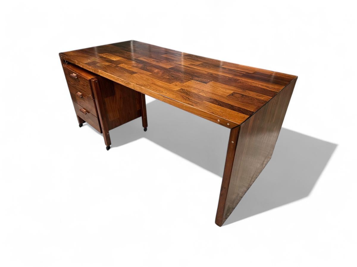 Available today, this desk with a file cabinet, designed by Jorge Zalszupin and produced by his company L’Atelier in the 1960s, highlights an innovative approach to Brazilian rosewood in a patchwork style. This technique, which involves a collage of