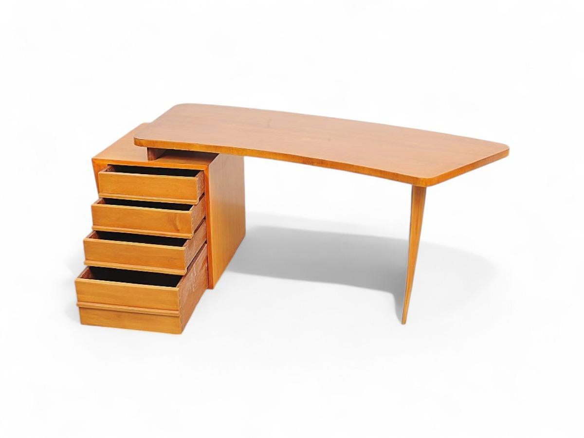 Ce remarquable bureau est fabriqué en bois ivoire et présente un plateau de forme organique, soutenu d'un côté par un pied elliptique et pointu et, de l'autre, par une colonne qui comprend trois tiroirs ainsi qu'un tiroir plus grand. Le bureau a été