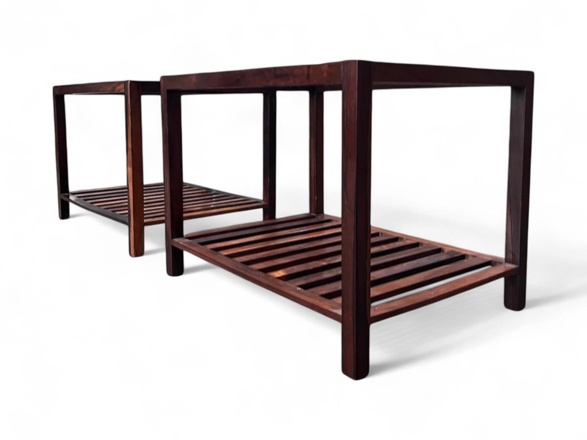 Estas elegantes mesas auxiliares rectangulares están fabricadas en madera noble y tienen un tablero de cristal. Tienen una estructura de dos niveles: el inferior presenta delicadas lamas, mientras que el superior exhibe el elegante cristal. El