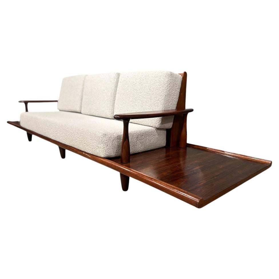 Questo divano è realizzato in legno di palissandro ed è stato tappezzato con un bellissimo bianco sporco.  boucle. Ciò che rende questo divano così unico sono i tavolini incorporati (anch'essi realizzati in palissandro). Il divano e i tavolini sono