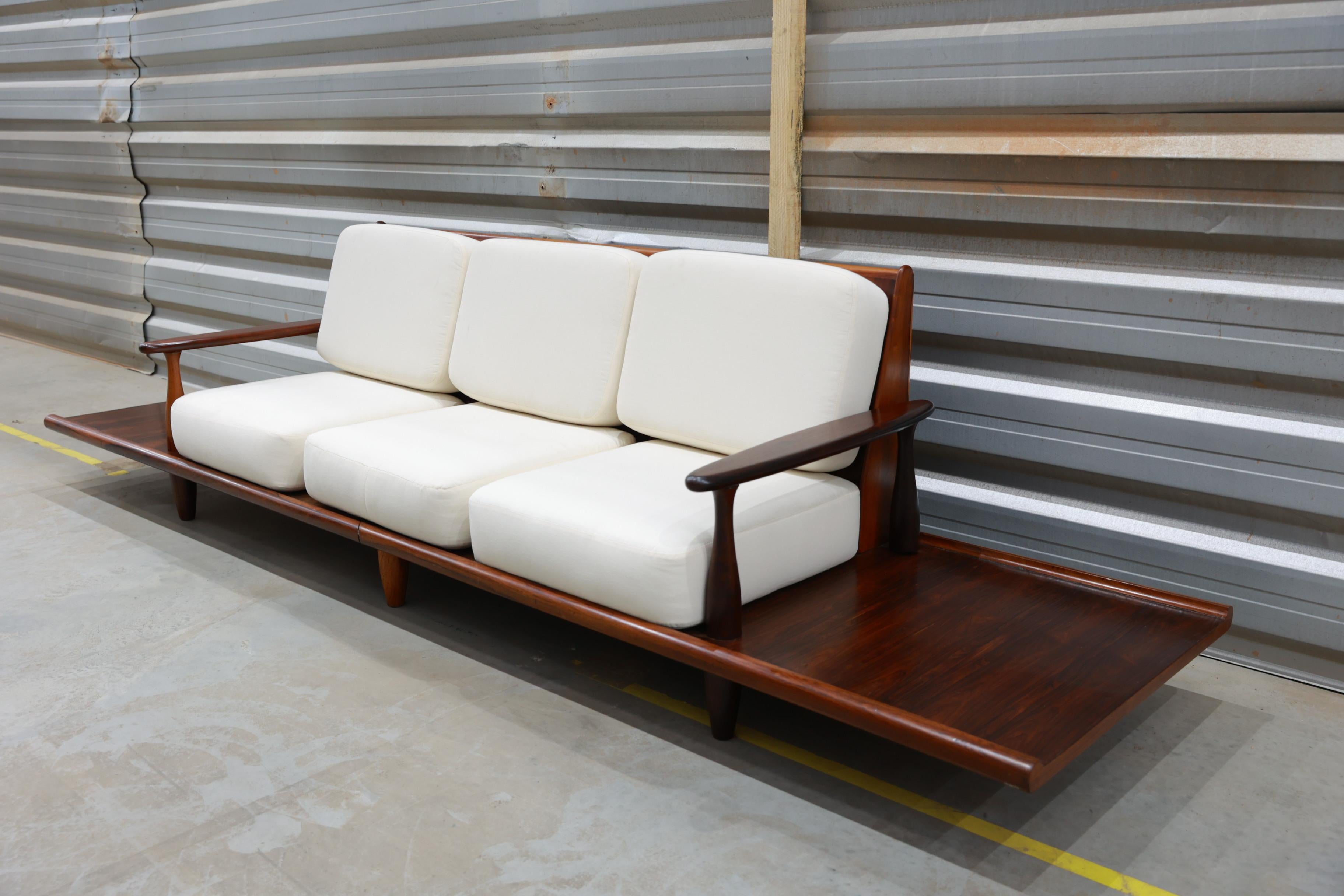 This sofa is made with Rosewood and it has been reupholstered with a beautiful off-white  fabric. What makes this sofa so unique are the built-in side tables (also made with Rosewood). The sofa and side tables are low, which allows for a comfortable