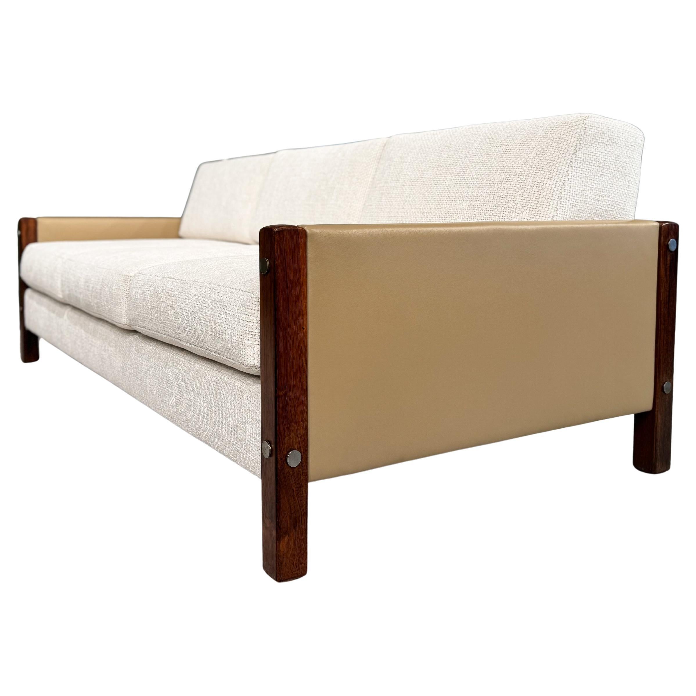 This sofa, named “Millor,” features a Brazilian rosewood frame, leather arm and back upholstery, loose cushions upholstered in a super soft textured off-white fabric and four chrome-finished legs. The wood has been refinished, and the seats