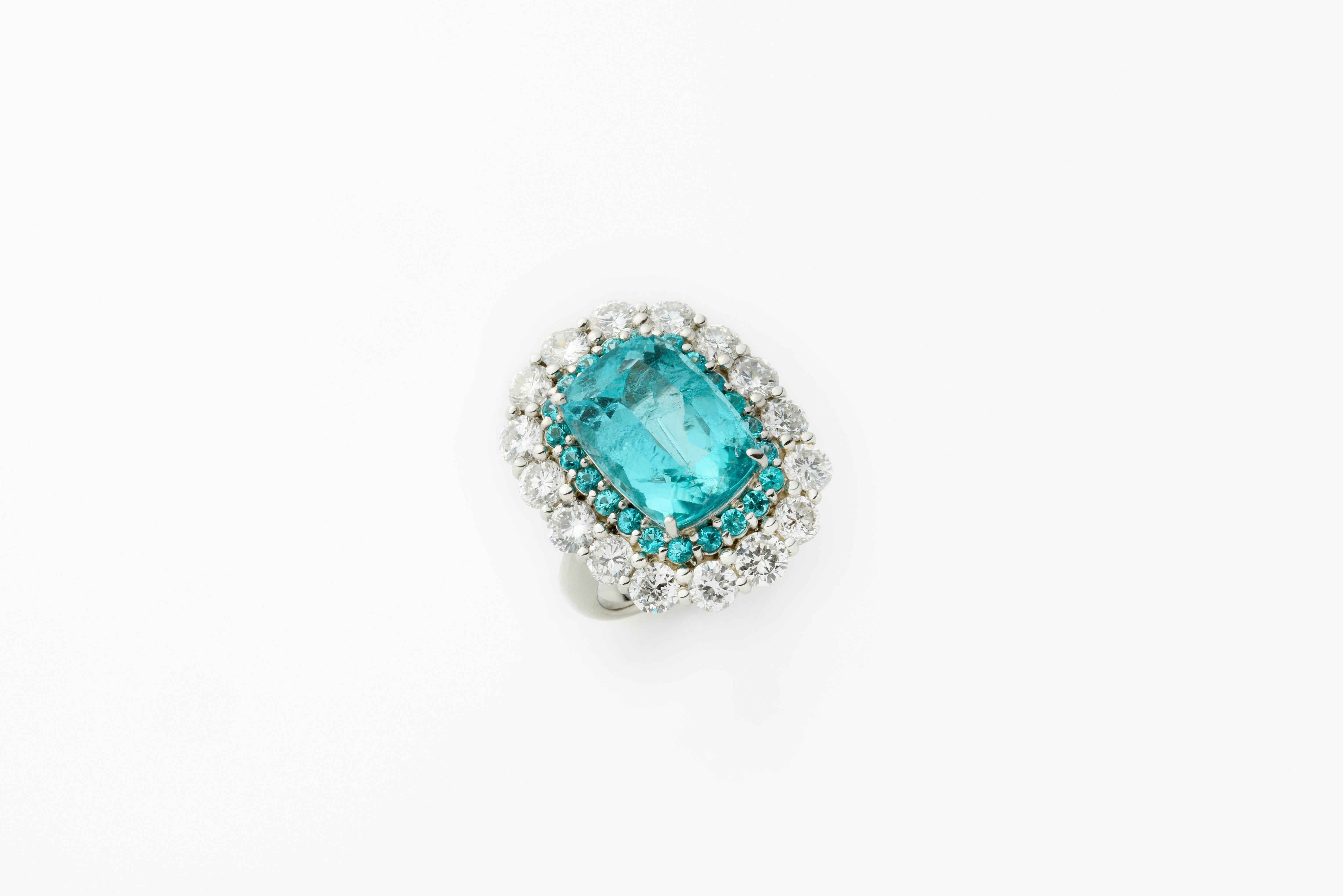 The sensational color, 8.99 carat Brazilian Paraiba tourmaline in the cocktail-style platinum ring. Both GIA & GRS Certified, This elegant, cushion-cut Paraiba is surrounded by two layers of stones: Brazilian Tourmaline stones and diamonds.  
This