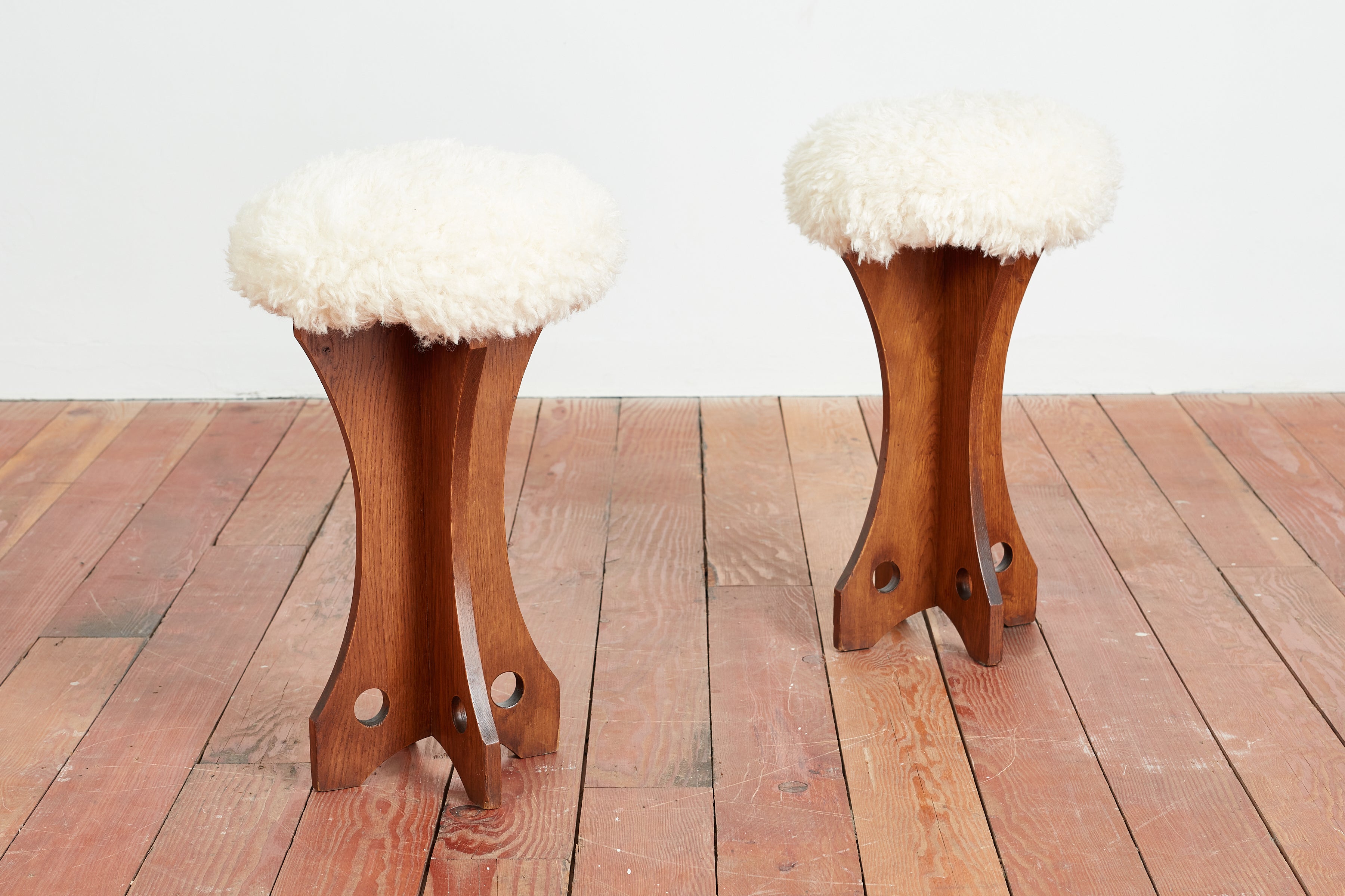 Unique pair of Brazilian-made poufs with wood angular wooden frames with circular geometric cut outs. 
The ottomans have been newly reupholstered in faux shearling. 