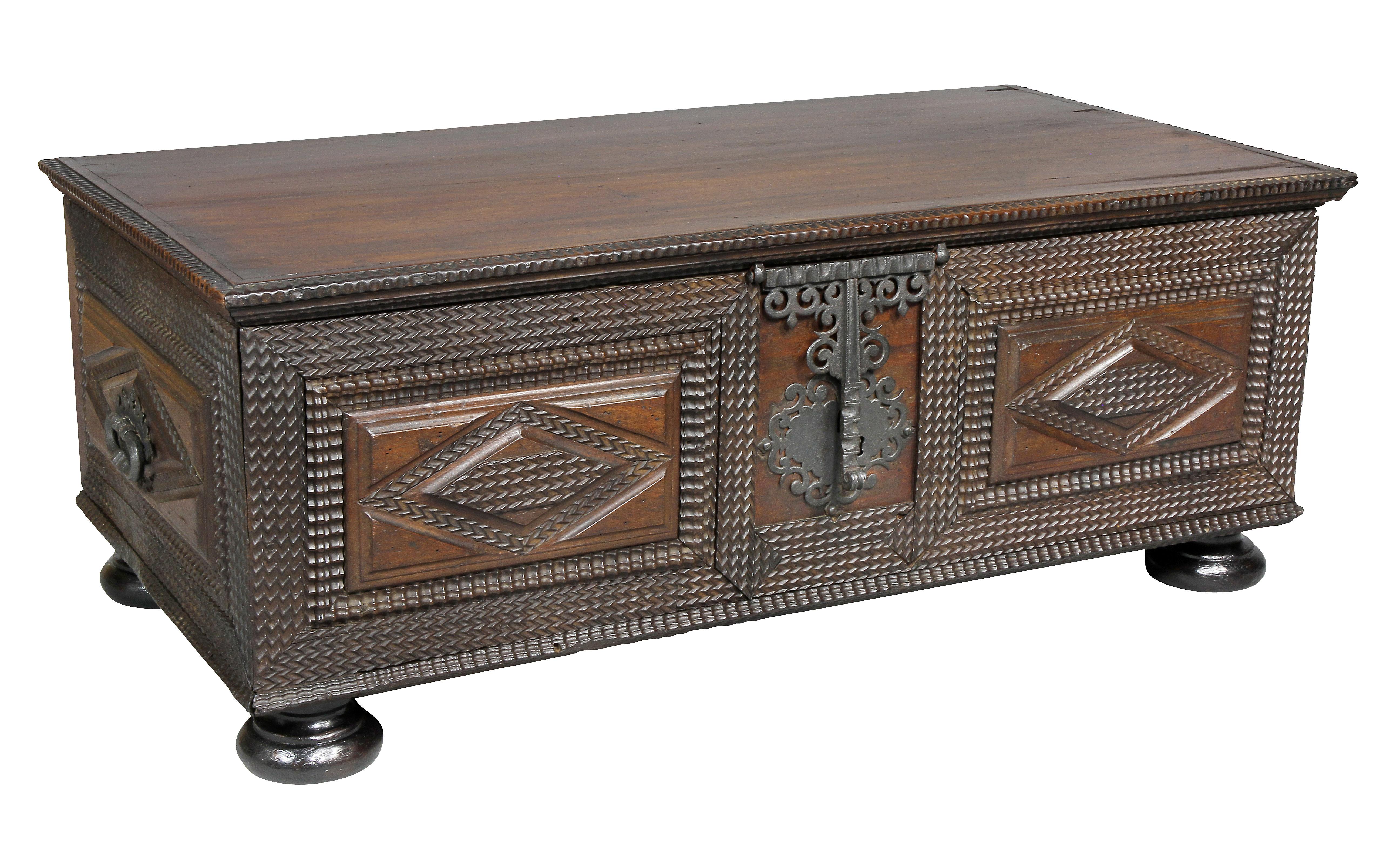 With rectangular hinged top over a case with two panels with diamond carved centers, elaborate wrought iron hinged latch and lock plate, side handles with carved diamond shape panels, bun feet.