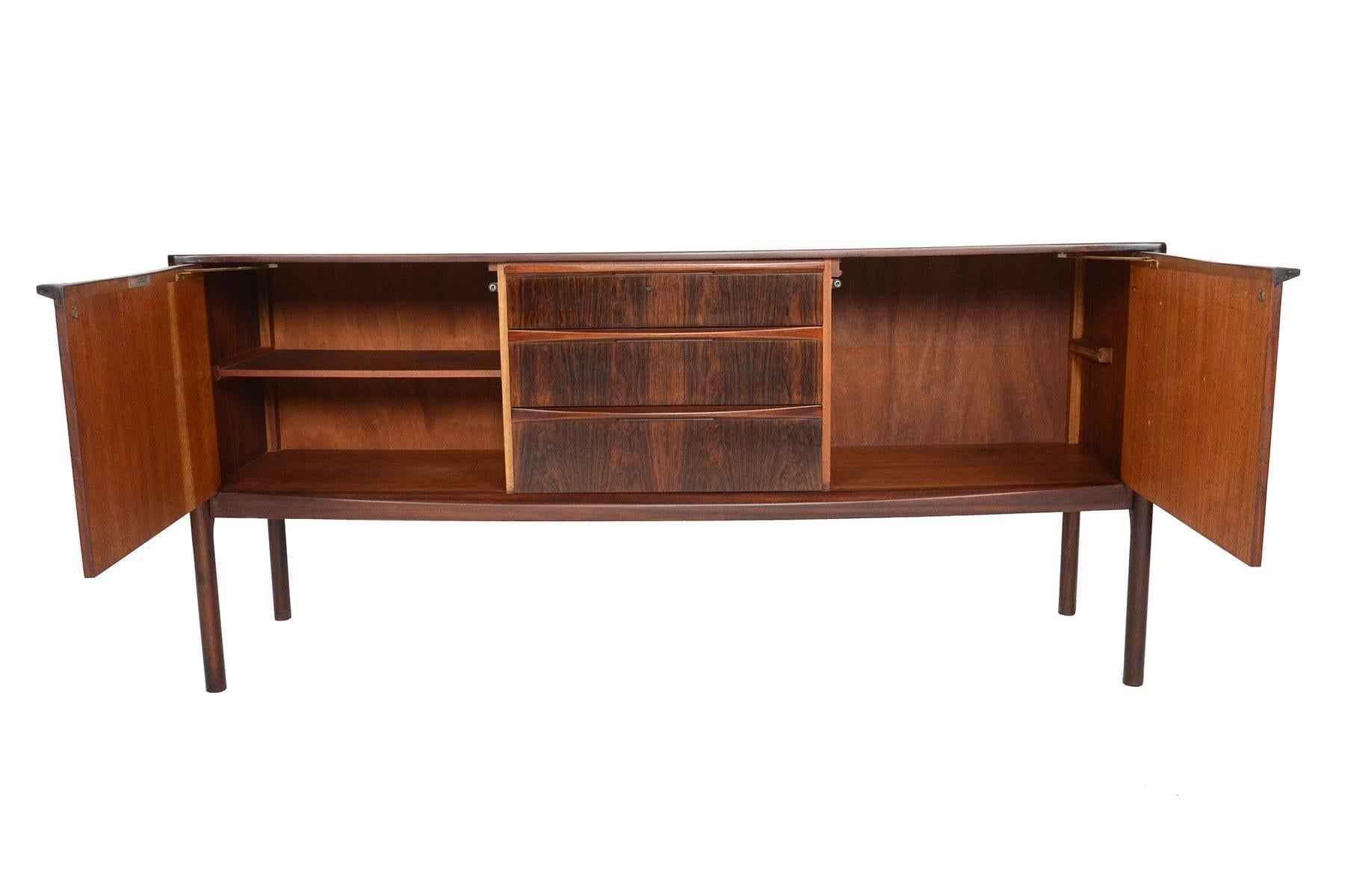This large, low line credenza was manufactured by A.H. McIntosh in the 1960s and is perfectly suited for any modern home. Cased in gorgeous Brazilian rosewood, this piece is accented by carved mahogany drawer pulls and bowed base. Left and right