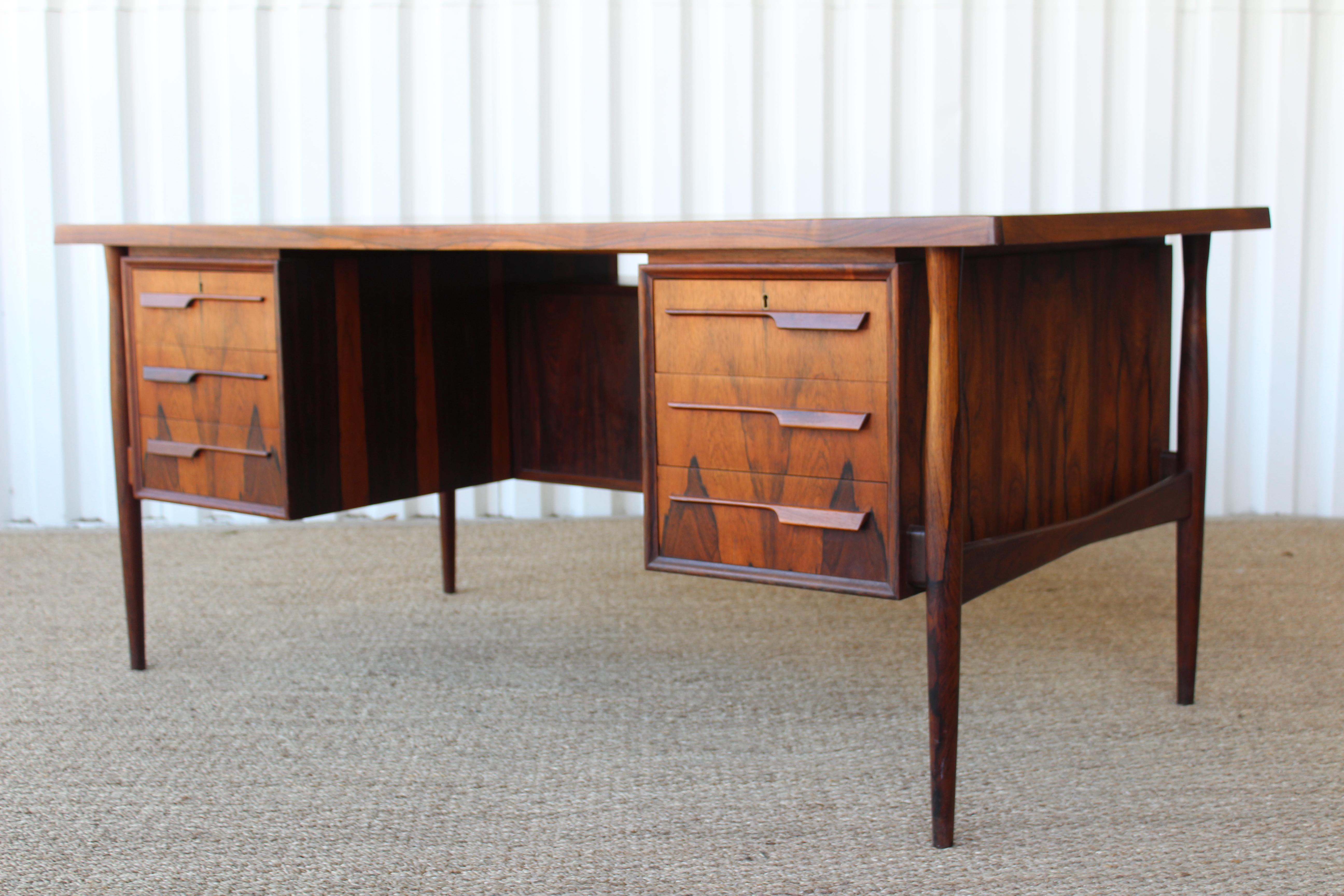 Danish modern desk in Brazilian rosewood. Five front drawers, two back compartments for storage and shelf for books in the back. Sculpted rosewood pulls. Recently refinished with some minor fading and surface wear on the top surface. Comes with a
