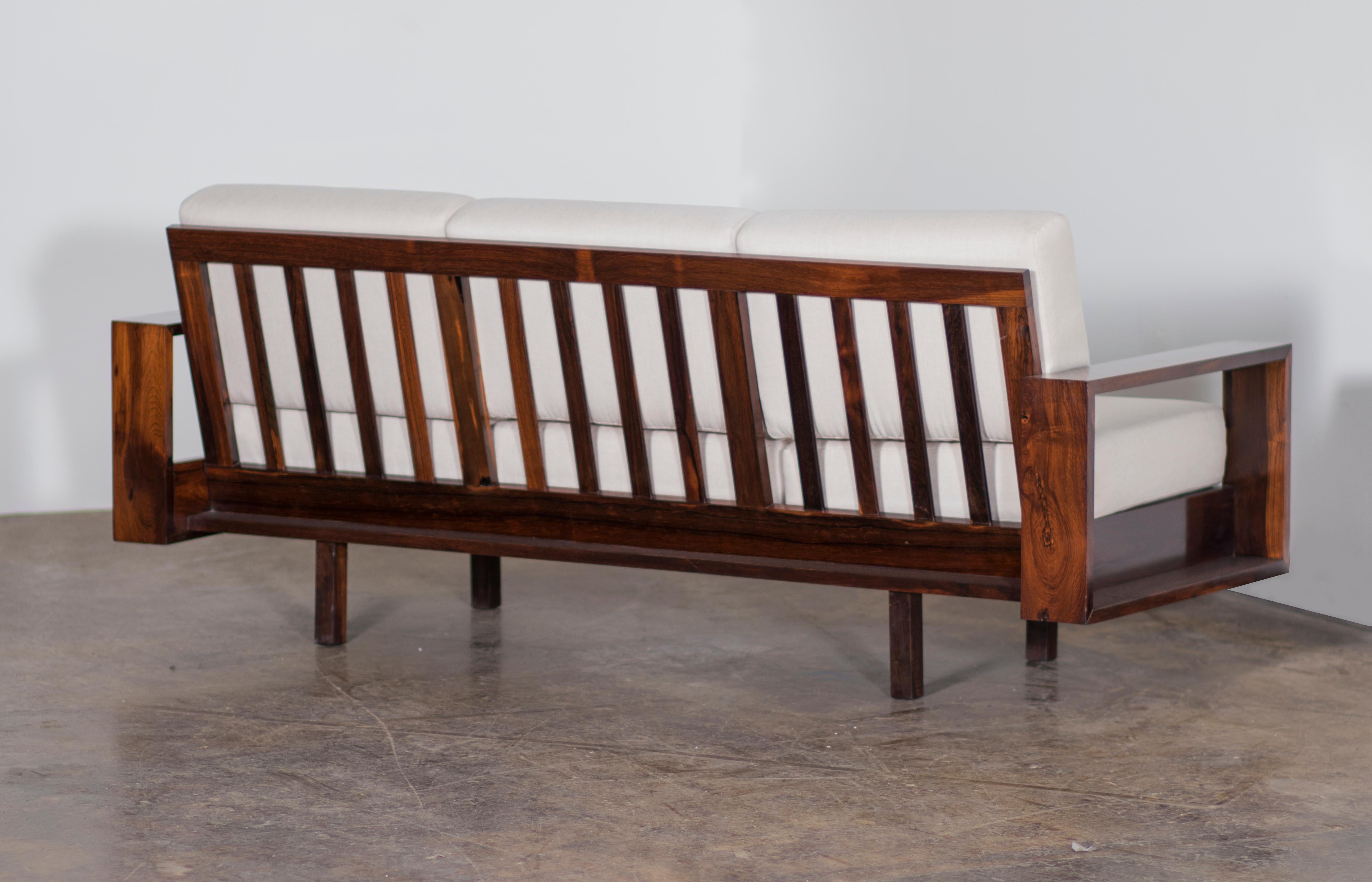 This beautiful sofa is made of solid Brazilian Rosewood (Jacaranda) and recently reupholstered in off white linen by the experienced craftsmen in our team. The armrests have a rectangular design, the back is composed of vertical slats, and the base