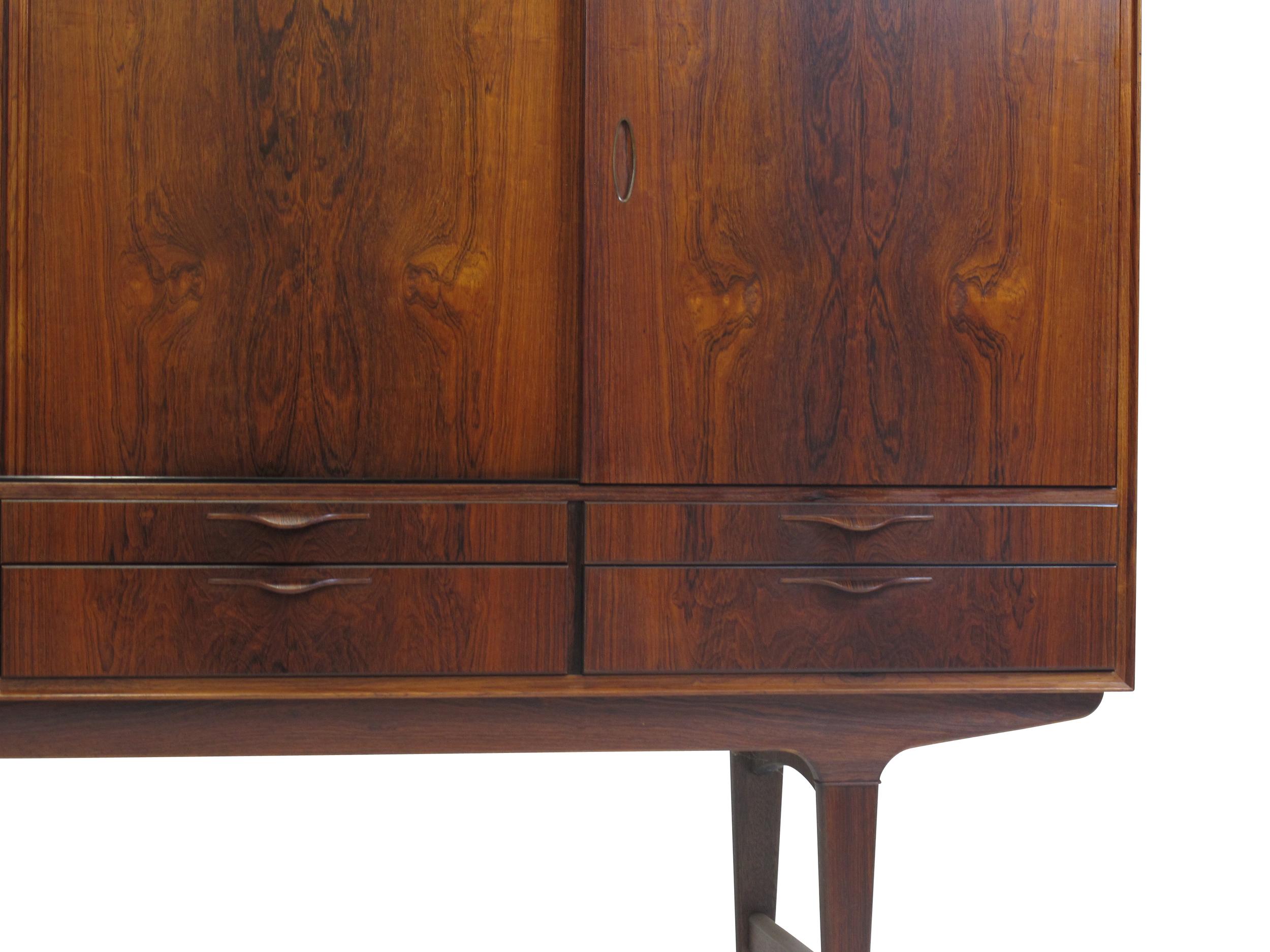 Brazilian rosewood credenza crafted of rosewood, four sliding doors with figured book-matched grain and sculpted pulls, over a series of six drawers raised in stilted legs. The cabinet interior is mahogany with adjustable shelves. The cabinet has