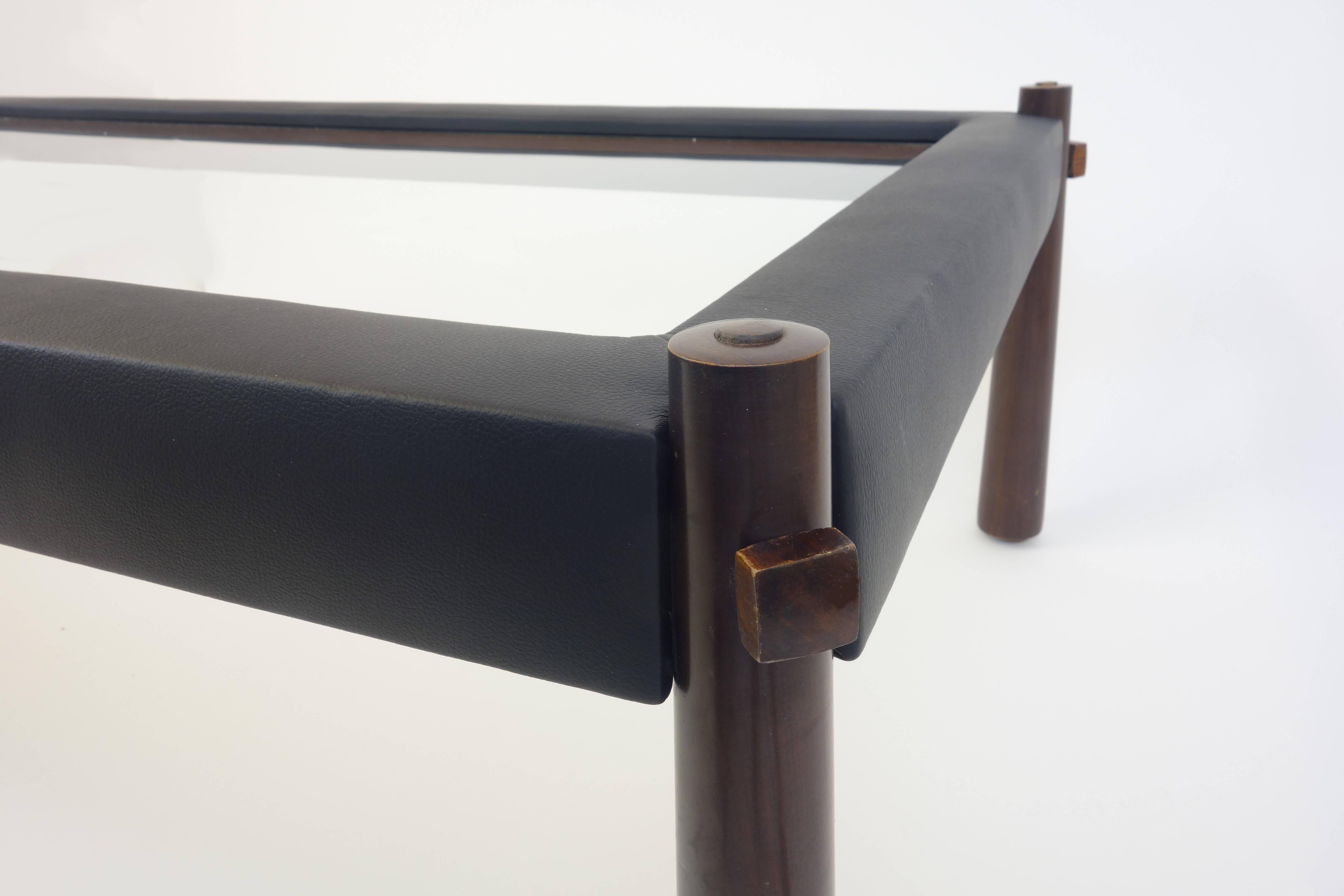 Une table d'appoint percutante conçue par Percival Lafer, Brésil, 1960. Un objet ferme et lourd, tapissé de cuir noir et complété par un plateau en verre à assise profonde. De plus, cet objet remarquable est élégamment surélevé par ses pieds en bois