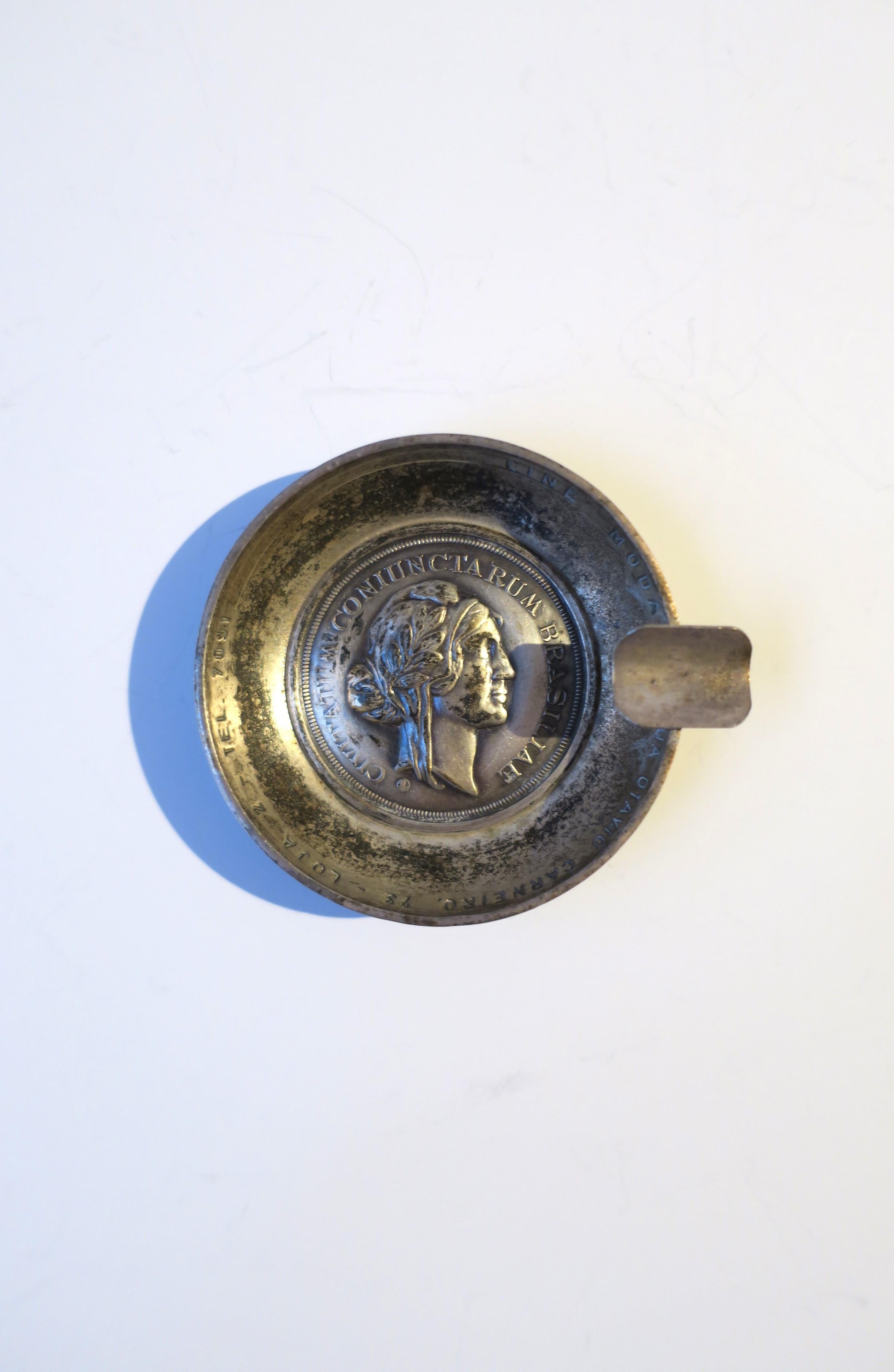 A silver plate and metal coin ashtray from Brazilian restaurant 'Cine Modas', circa mid-20th century, Brazil. Restaurant information is embossed around top inside rim, center coin is a female head bust representative of Brazilian rum company