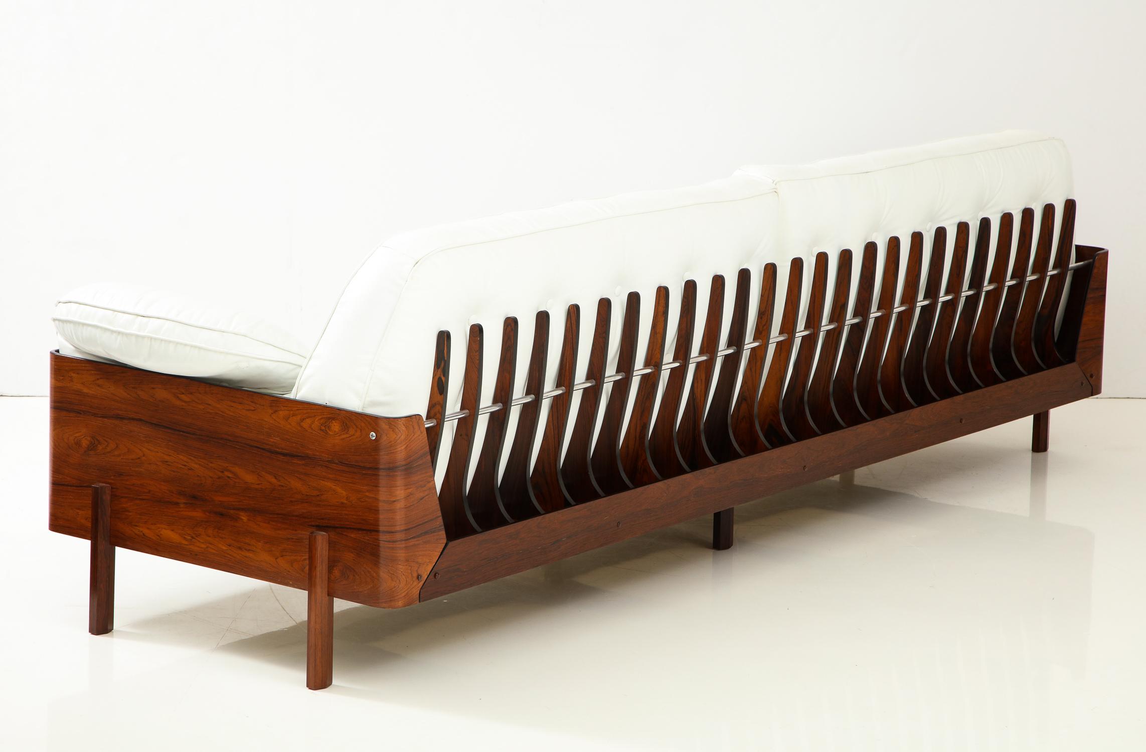 Eight foot long sofa in beautifully figured Jacaranda wood with a series of skeletal fins along the back connected with an aluminum rod, and original white leather cushions. A visually impressive design made in Sao Paulo, Brazil, circa 1965. A rare