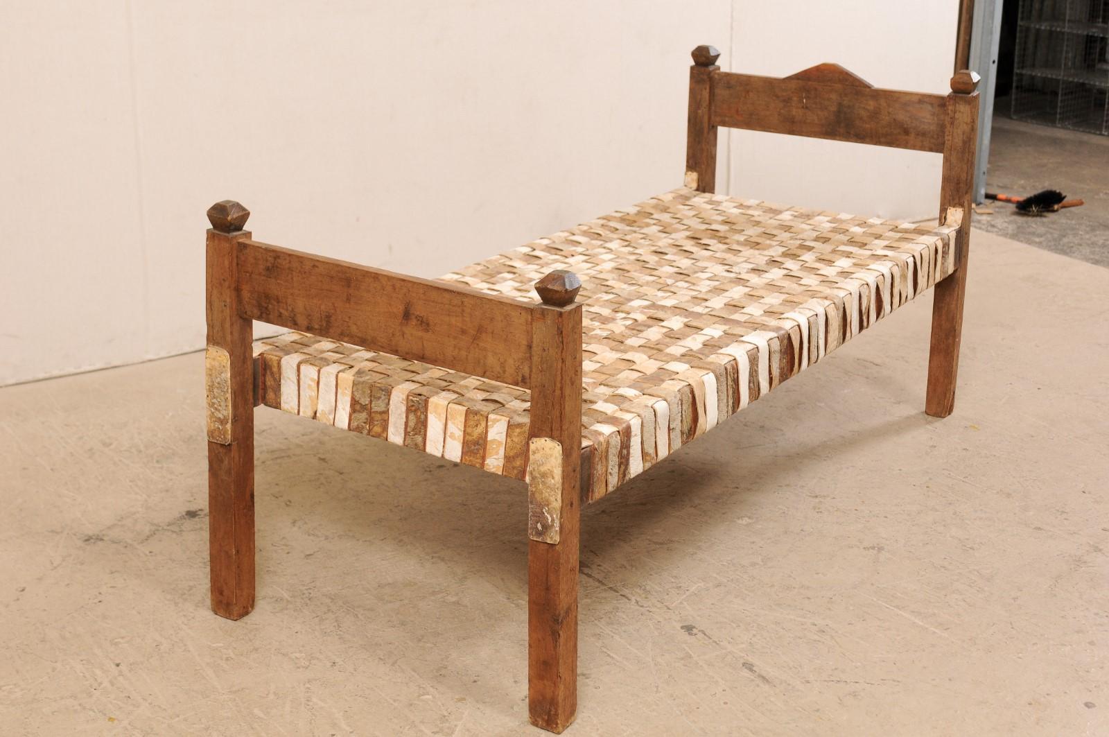 A Brazilian single woven-leather and wood daybed or bench. This Brazilian daybed from the mid-20th century has a great rustic feel with it's bucolic frame and leather strip seat. The wooden headboard is comprised by a single board, styled with a