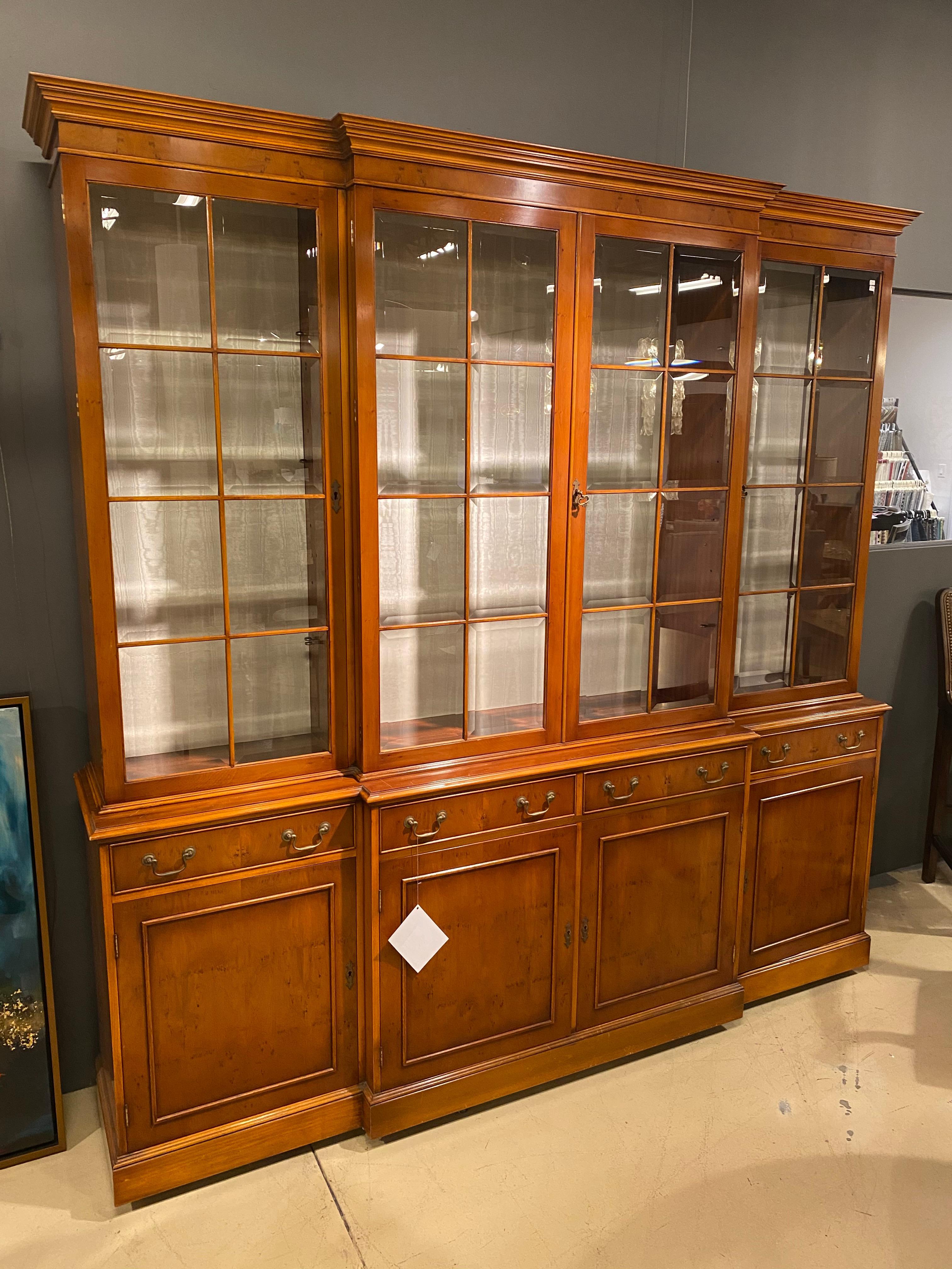 A grand English breakfront display bookcase in Georgian styling crafted in Yew by Bevan Funnel. Eight beveled glass panels in the upper doors along with glass shelves and the off white silk moire backing make this an excellent showcase for treasured