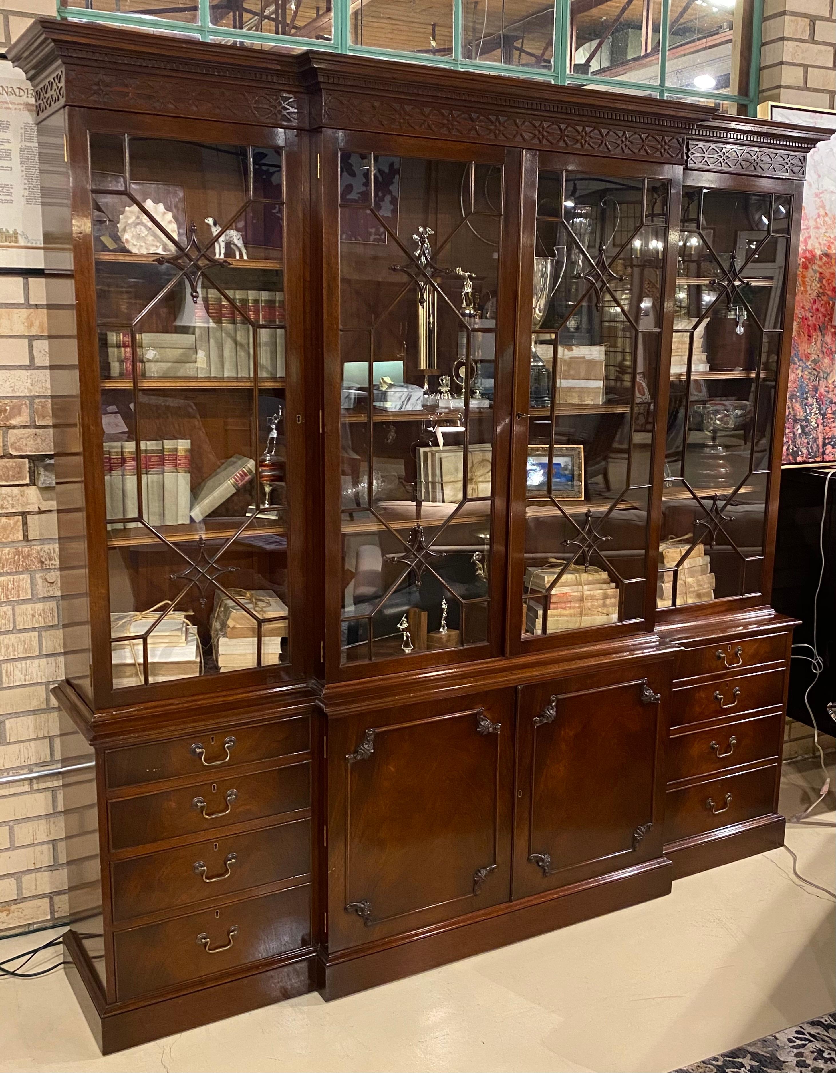 A traditional Georgian style English breakfront bookcase in mahogany. Classic 18th century detail and styling. Individual hand glazed upper doors with carved details add to the impressive nature of this cabinet. The broken arch swans neck pediment