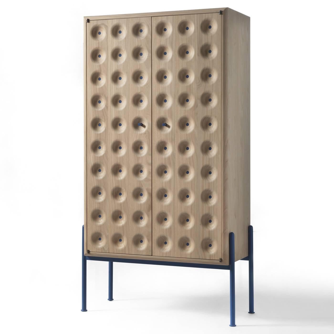 This exquisite cabinet has a skin-like surface whose texture invites a tactile experience. The Minimalist legs in iron varnished in pale blue support an imposing two-door cabinet in chestnut wood. The handles are in iron with the same pale blue