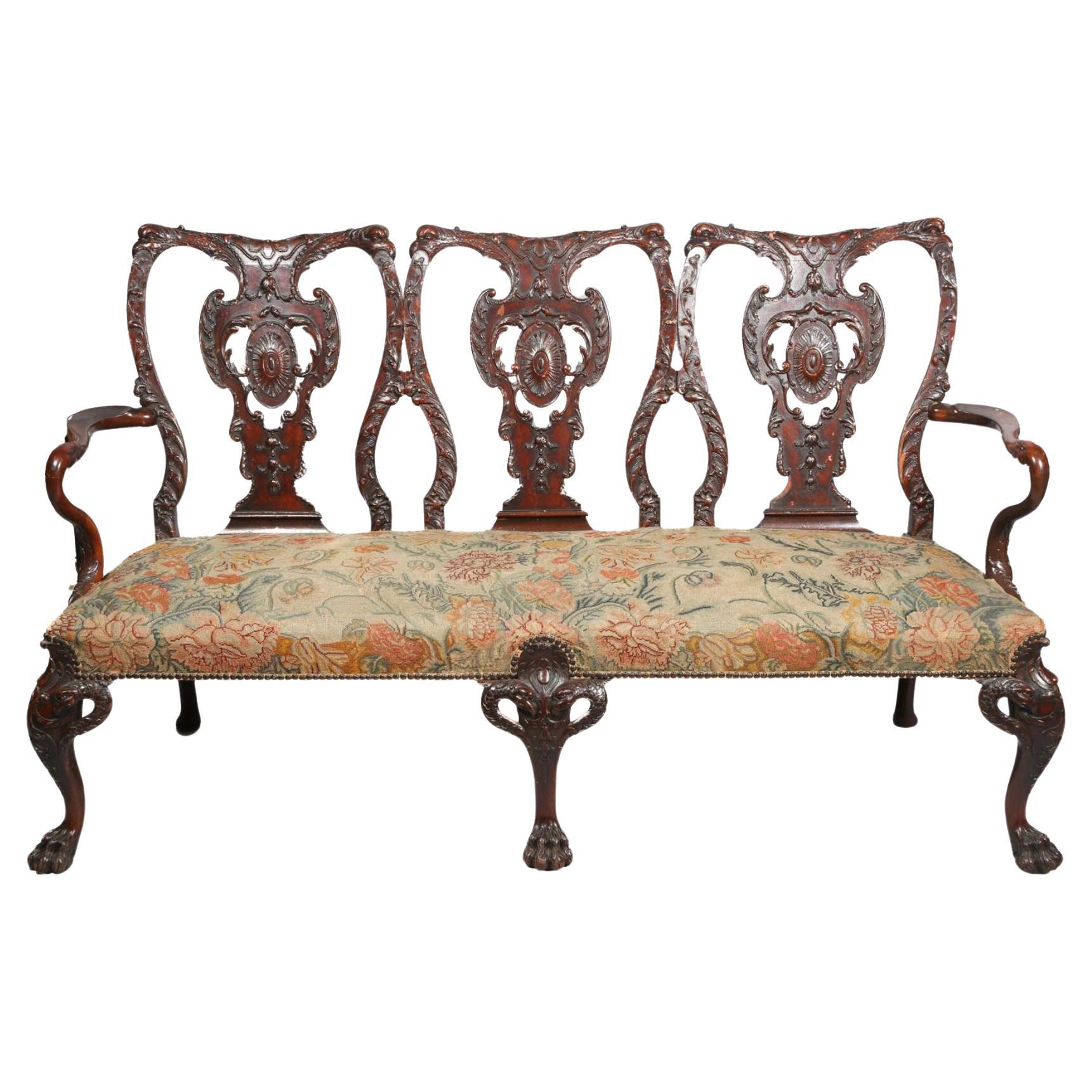 George II Revival triple back settee was created in the style of the beloved Thomas Chippendale. From the scaled and scalloped back and zoomorphic armrests to the hairy ball-and-claw feet, the quality of the carving is deep and richly detailed.