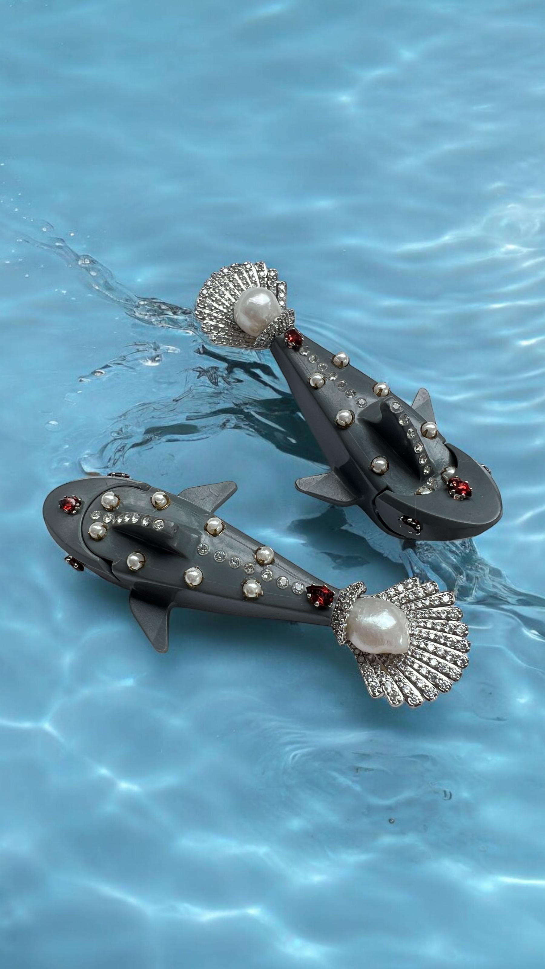 These one-of-a- kind earrings bring a playful twist to high-end jewelry, featuring Lego shark figures embedded with Swarovski crystals, pearls, and natural garnets. The shark's fin, masterfully crafted into a white gold-plated seashell shape,