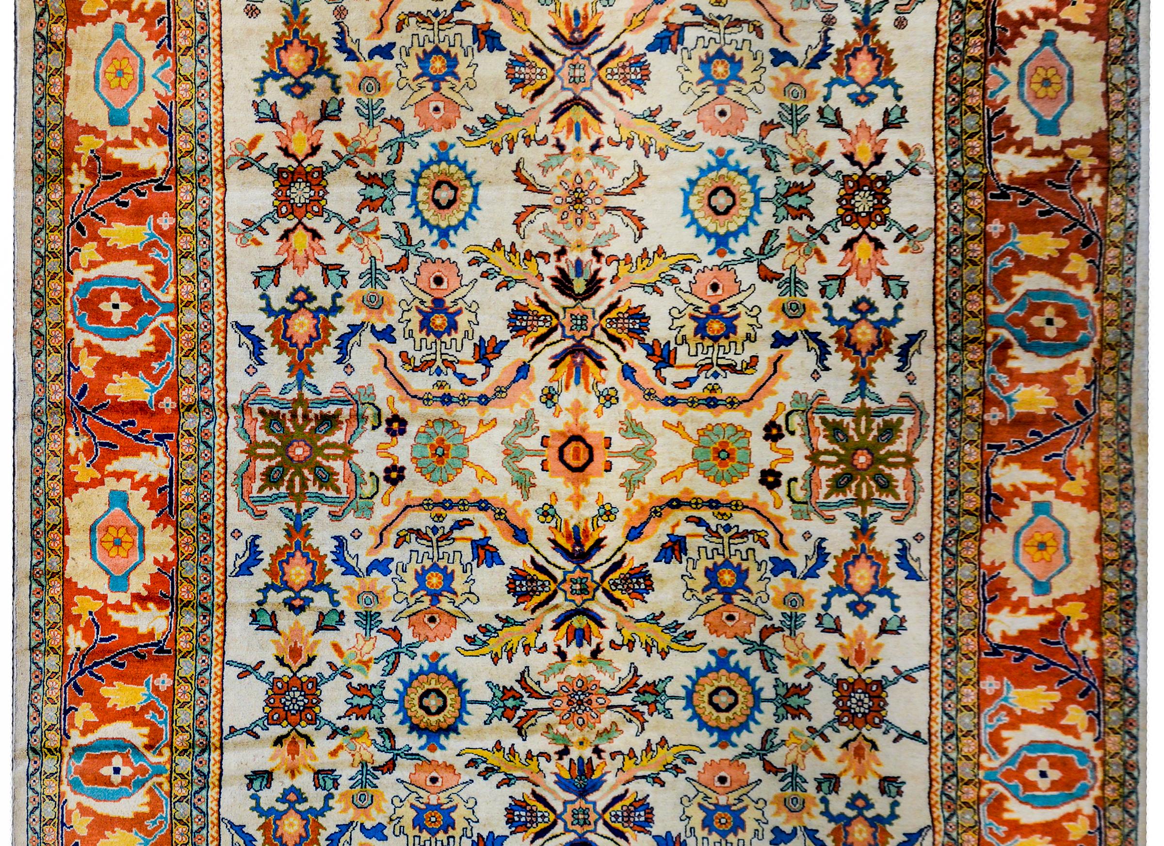 A breathtaking mid-20th century Persian Sultanabad rug with a large-scale mirrored floral patterned field woven in crimson, gold, green, pink, and indigo on a cream colored background, surrounded by a wide large-scale floral and scrolling vine