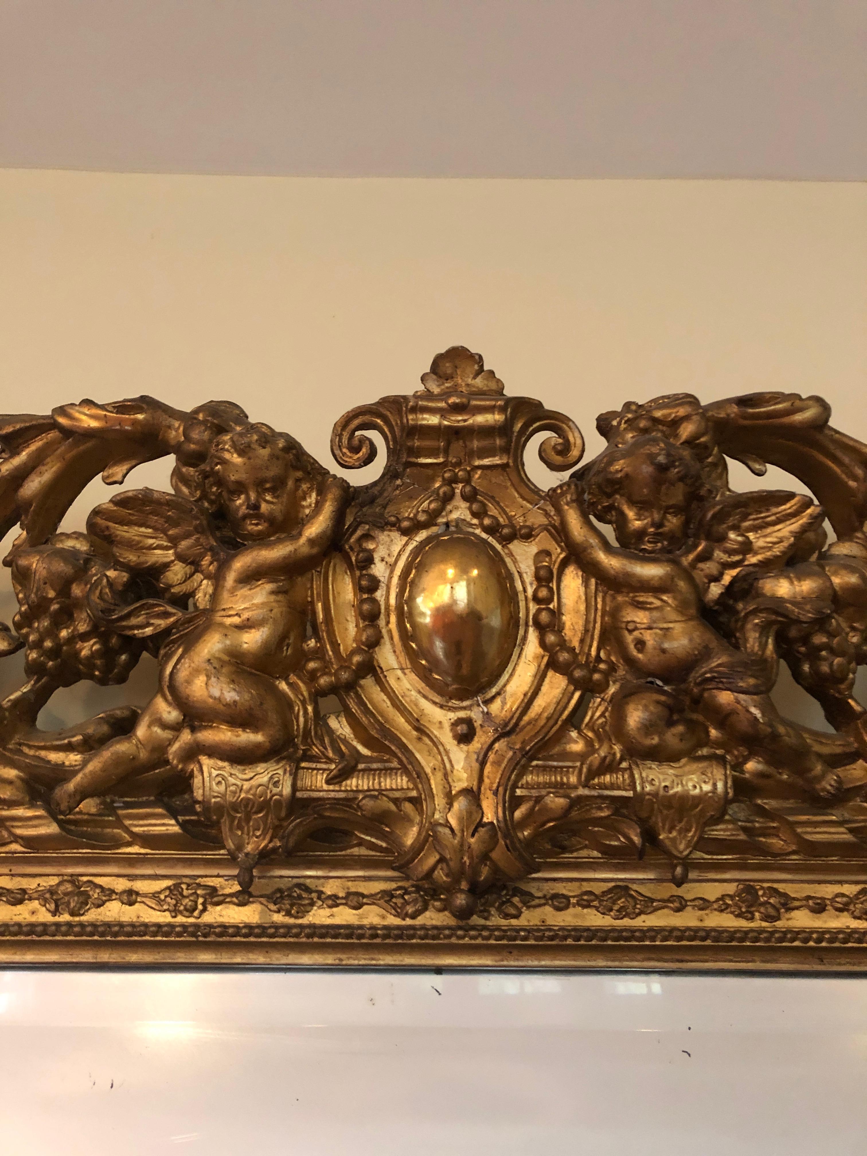 A gargantuan very impressive ornate giltwood mirror having romantic central shield at the top with two putti, lots of curlicues and fancy carvings and a huge naturally aged beveled mirror. Some losses to giltwood as shown in photos.