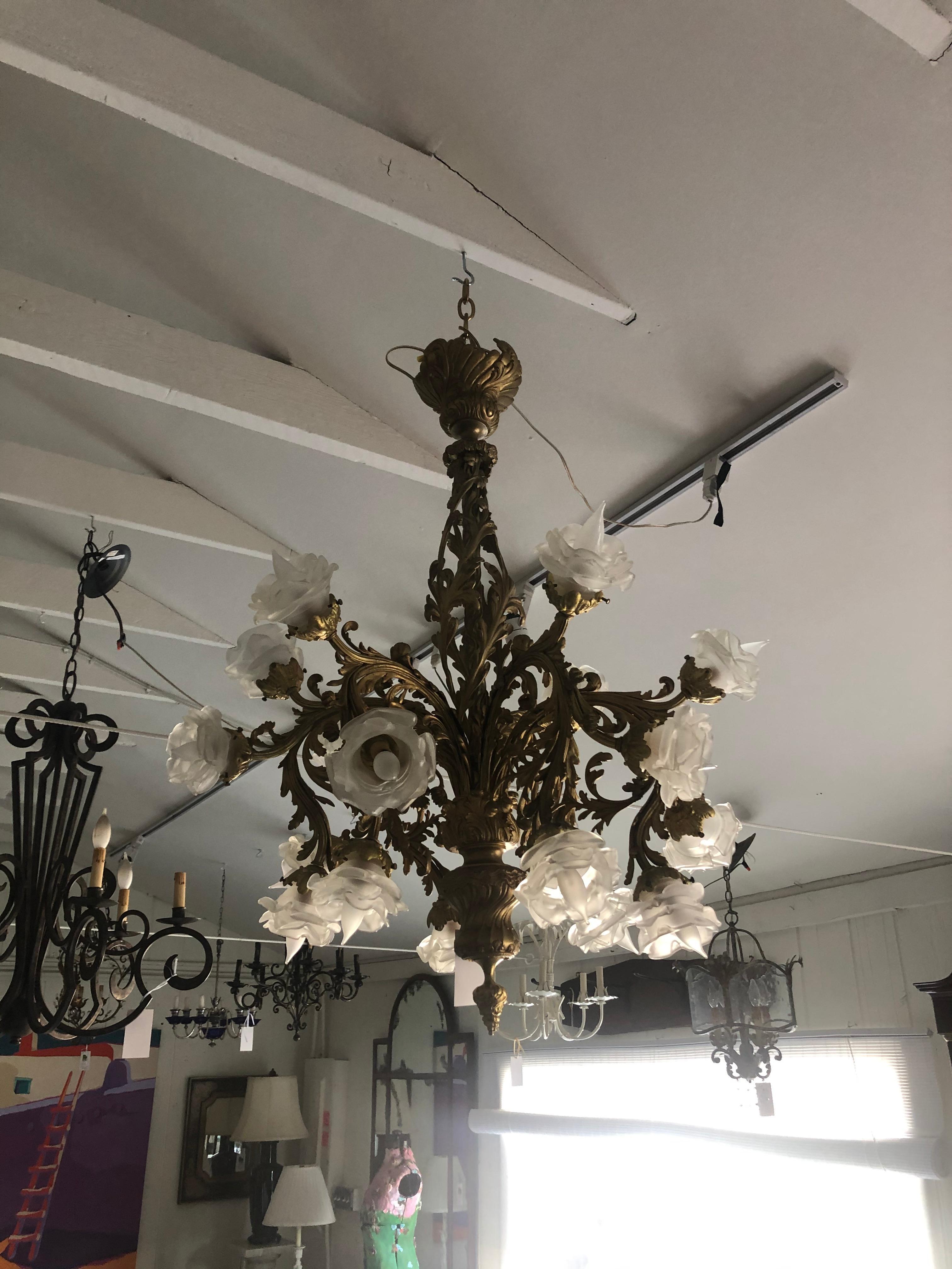 An ornate French Rococo style relief cast gilt bronze 18-light chandelier having frosted glass floral shades in the style of Lalique.