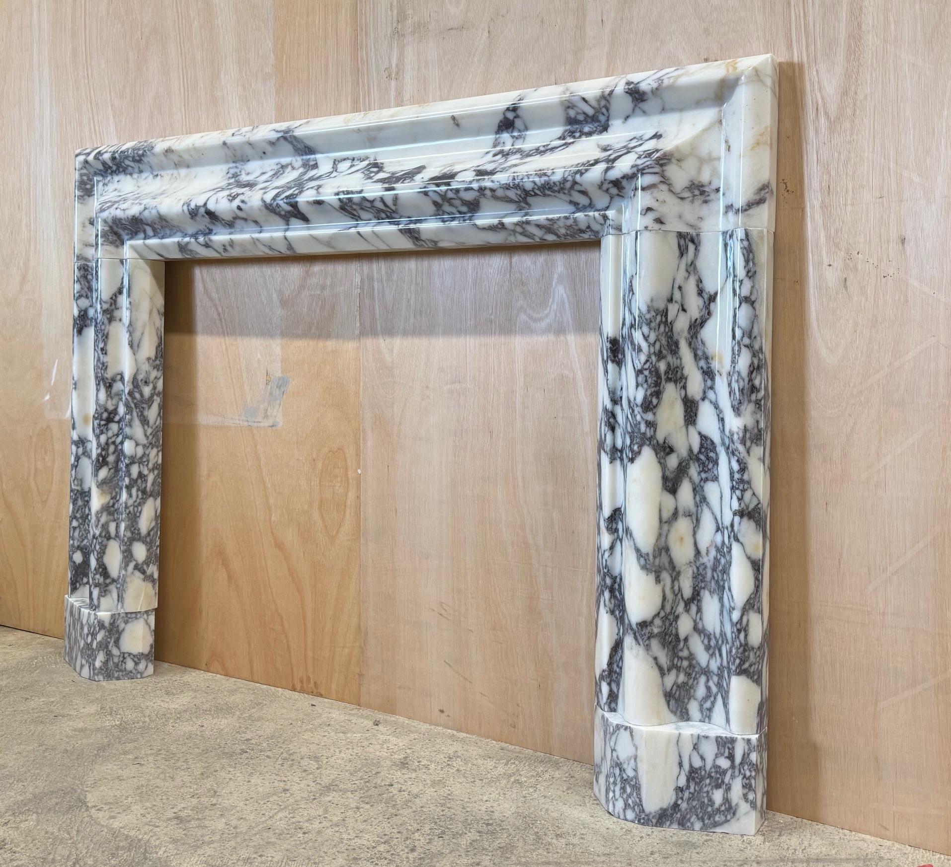 A large marble bolection fire surround of generous proportions.

The wide and simplified bolection moulded frame rests on plain angled plinths.
Carved in the solid from a block of beautifully figured, Breccia viola marble, hand selected in Italy by
