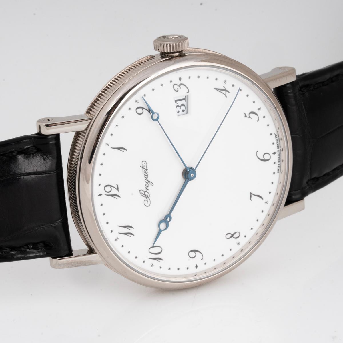 A Classique 38mm wristwatch in white gold by Breguet. Features a white enamel dial with a date display at 3 o'clock, blued-steel Breguet hands, and a fluted white gold case band.

Equipped with a black leather Breguet strap and a white gold pin